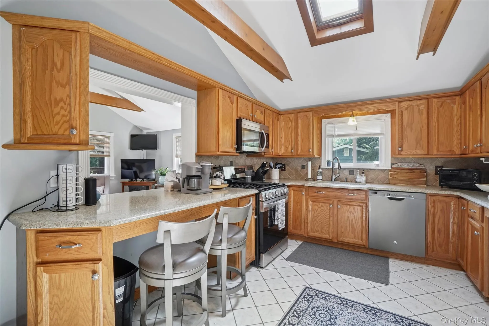Kitchen with appliances with stainless steel finishes, a skylight, a kitchen bar, light tile patterned floors, and light stone countertops Kitchen with appliances with stainless steel finishes, a skylight, a kitchen bar, light tile patterned floors, and light stone countertops