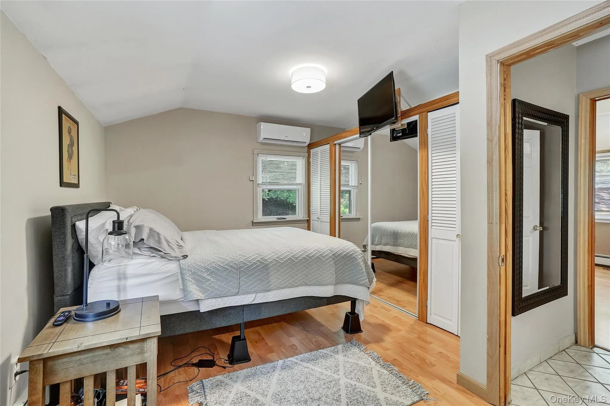 Bedroom with light wood-style floors, vaulted ceiling, a closet, and a wall mounted air conditioner Bedroom with light wood-style floors, vaulted ceiling, a closet, and a wall mounted air conditioner