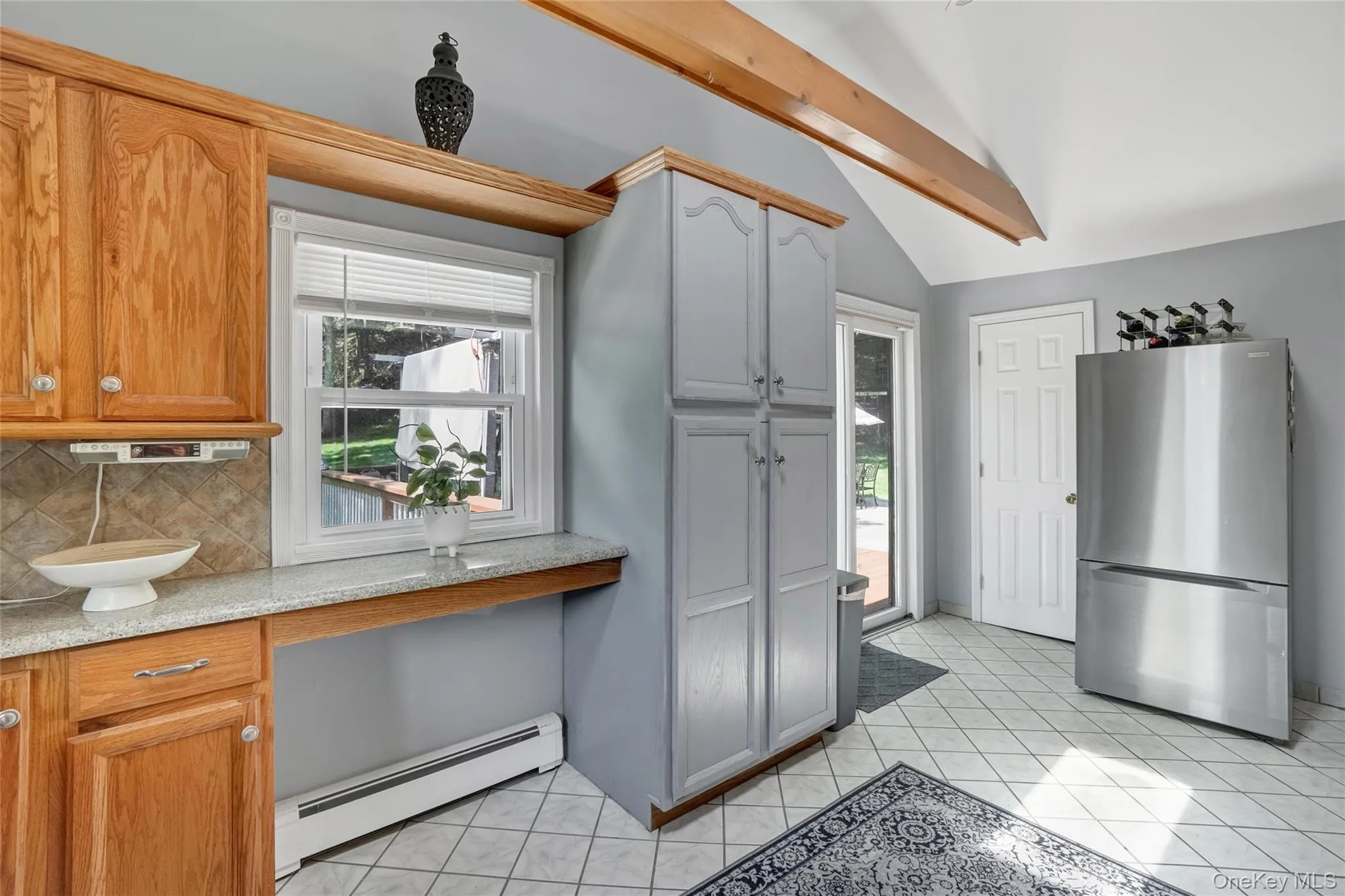 Kitchen featuring freestanding refrigerator, a baseboard heating unit, healthy amount of natural light, and tasteful backsplash Kitchen featuring freestanding refrigerator, a baseboard heating unit, healthy amount of natural light, and tasteful backsplash