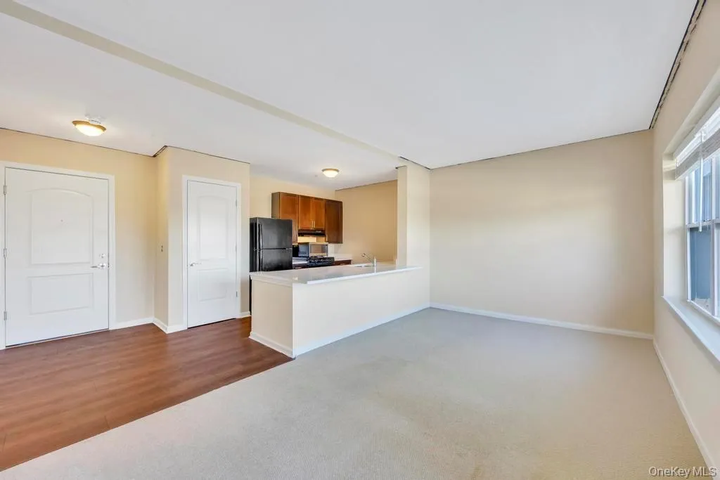 Kitchen featuring light countertops, brown cabinetry, dark colored carpet, open floor plan, and freestanding refrigerator Kitchen featuring light countertops, brown cabinetry, dark colored carpet, open floor plan, and freestanding refrigerator