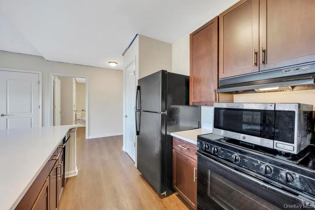 Kitchen with brown cabinets, black appliances, under cabinet range hood, and light wood finished floors Kitchen with brown cabinets, black appliances, under cabinet range hood, and light wood finished floors
