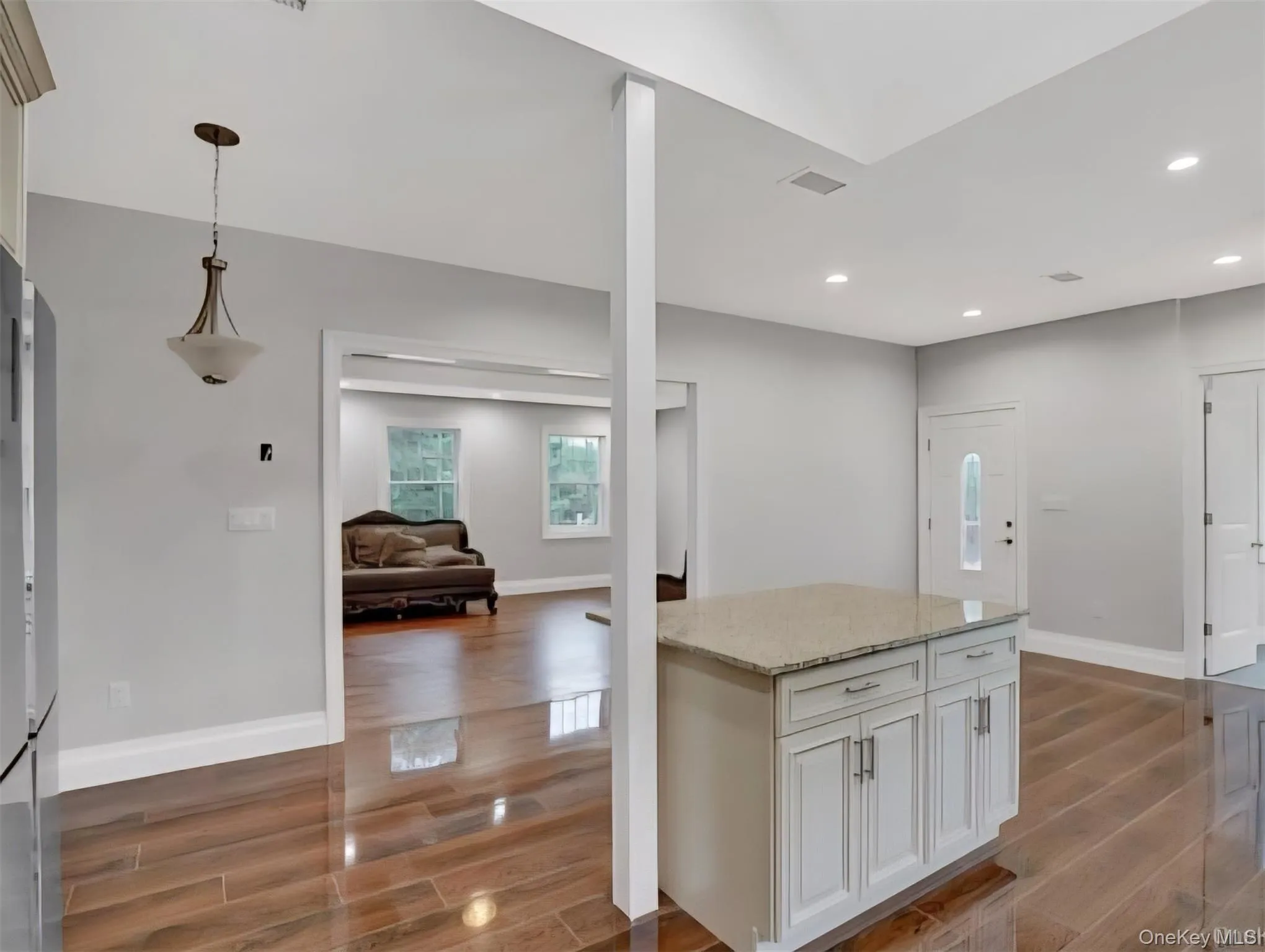 Kitchen with light stone countertops, wood tiled floors, white cabinets, hanging light fixtures, and open floor plan Kitchen with light stone countertops, wood tiled floors, white cabinets, hanging light fixtures, and open floor plan