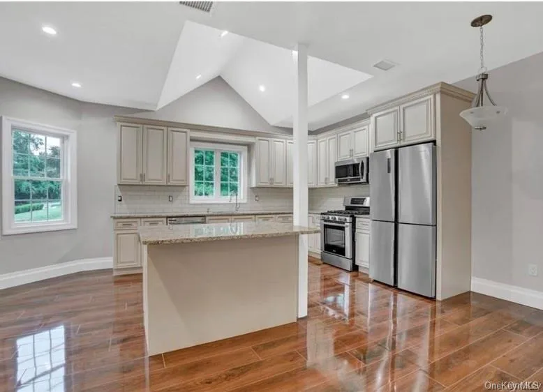 Kitchen featuring appliances with stainless steel finishes, light stone countertops, vaulted ceiling, hanging light fixtures, and decorative backsplash Kitchen featuring appliances with stainless steel finishes, light stone countertops, vaulted ceiling, hanging light fixtures, and decorative backsplash