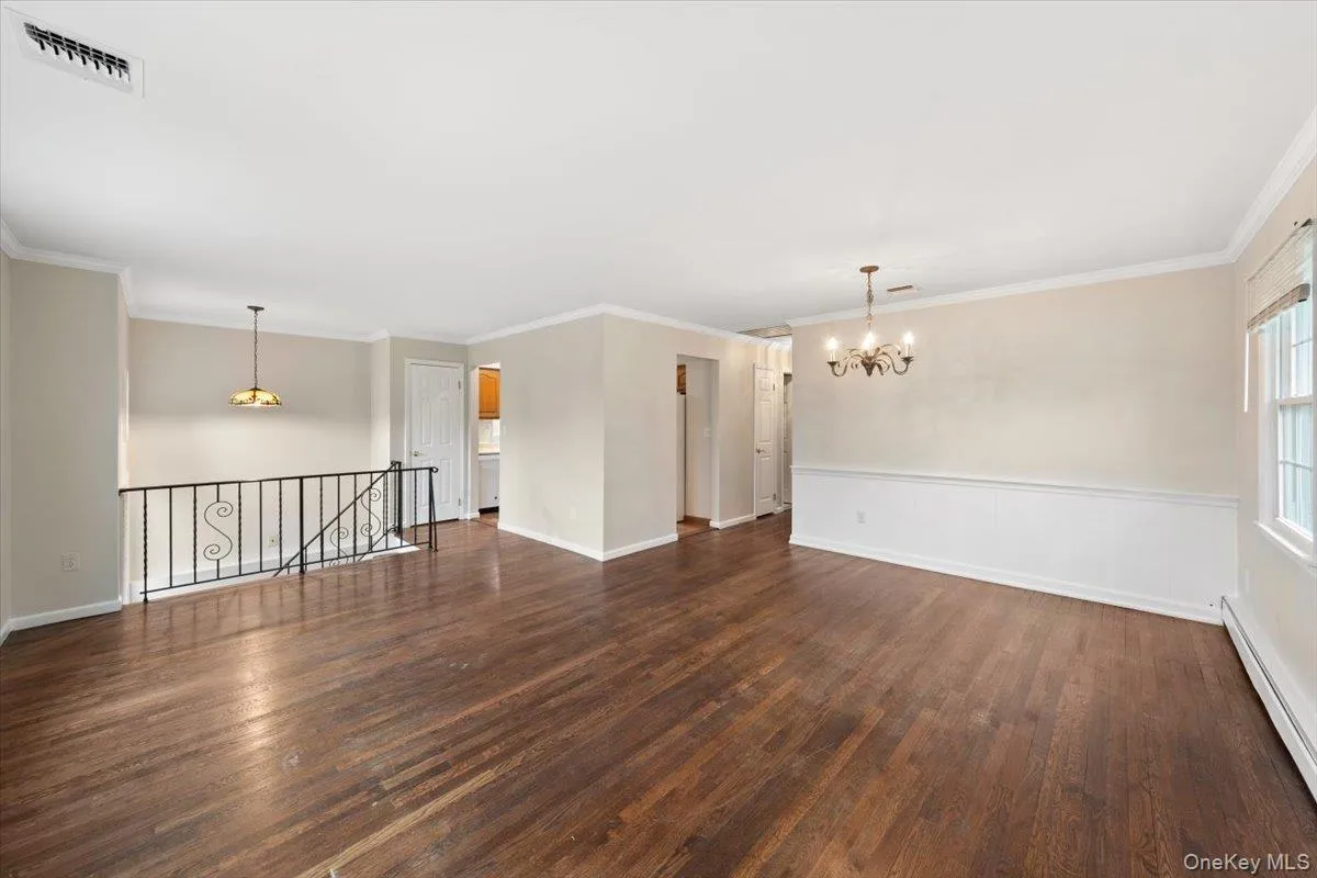 Spare room with a chandelier, a baseboard radiator, crown molding, and dark wood-style flooring Spare room with a chandelier, a baseboard radiator, crown molding, and dark wood-style flooring