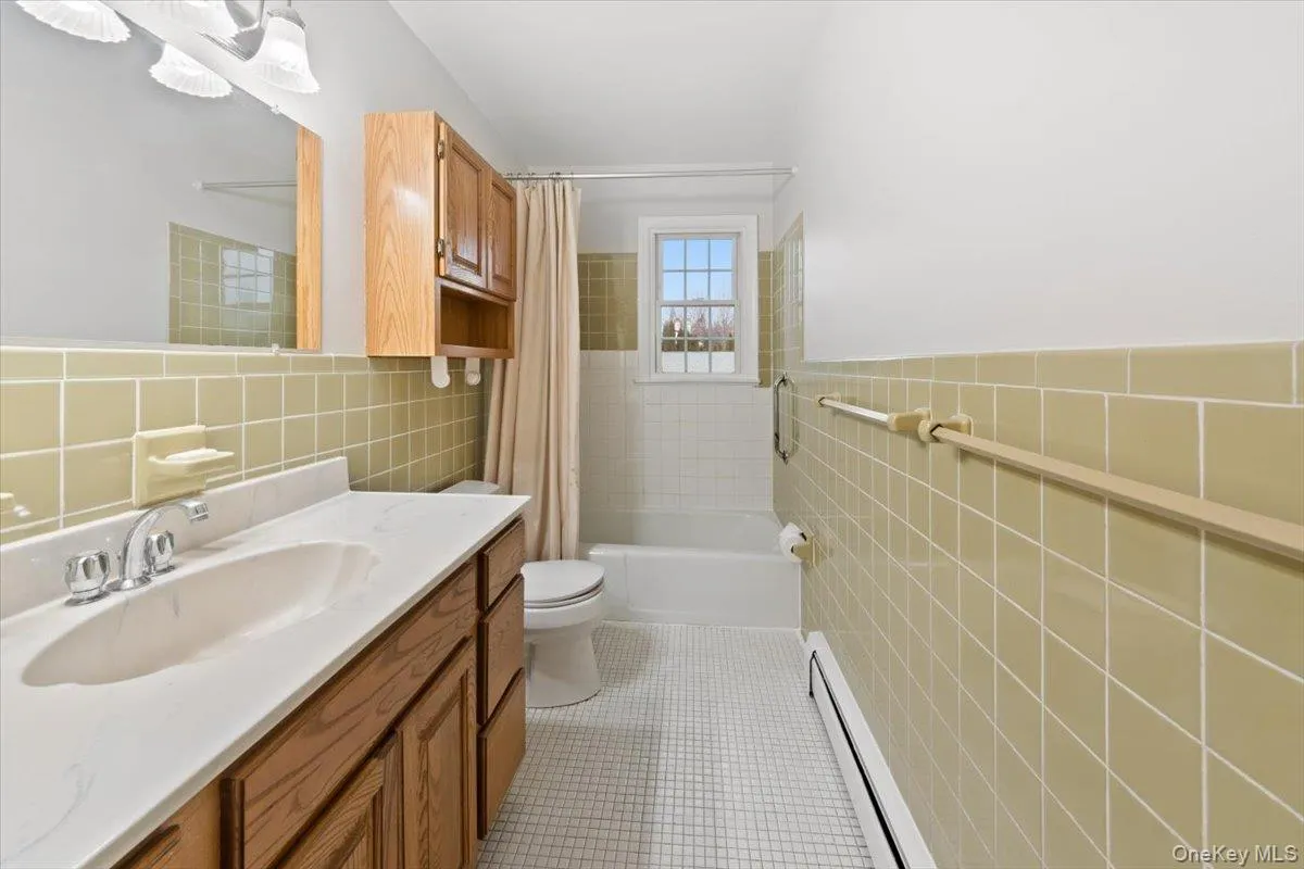Full upstair's bathroom featuring tile walls, baseboard heating, vanity, shower / bath combo with shower curtain, Full upstair's bathroom featuring tile walls, baseboard heating, vanity, shower / bath combo with shower curtain,