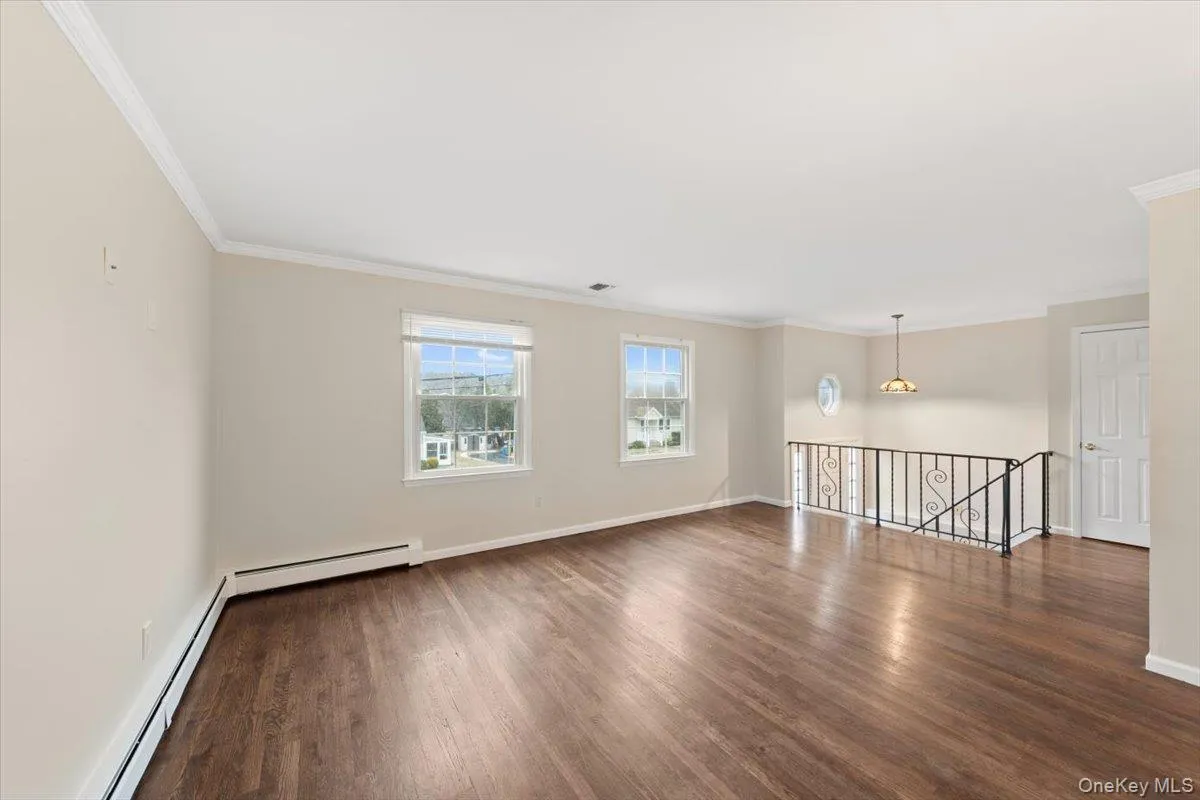 Unfurnished room featuring baseboard heating, crown molding, and dark wood-style floors Unfurnished room featuring baseboard heating, crown molding, and dark wood-style floors