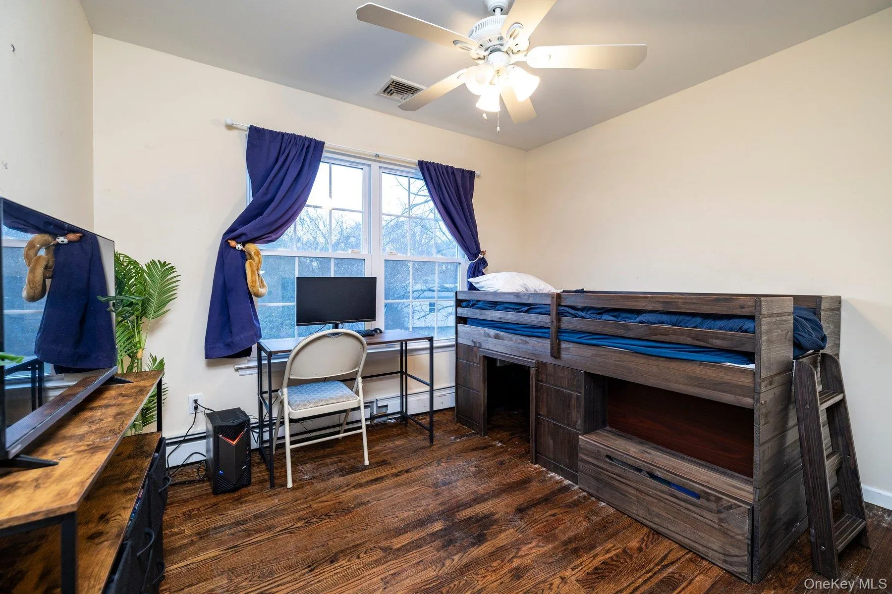 Bedroom with a desk, dark wood-style flooring, a ceiling fan, and a baseboard radiator Bedroom with a desk, dark wood-style flooring, a ceiling fan, and a baseboard radiator