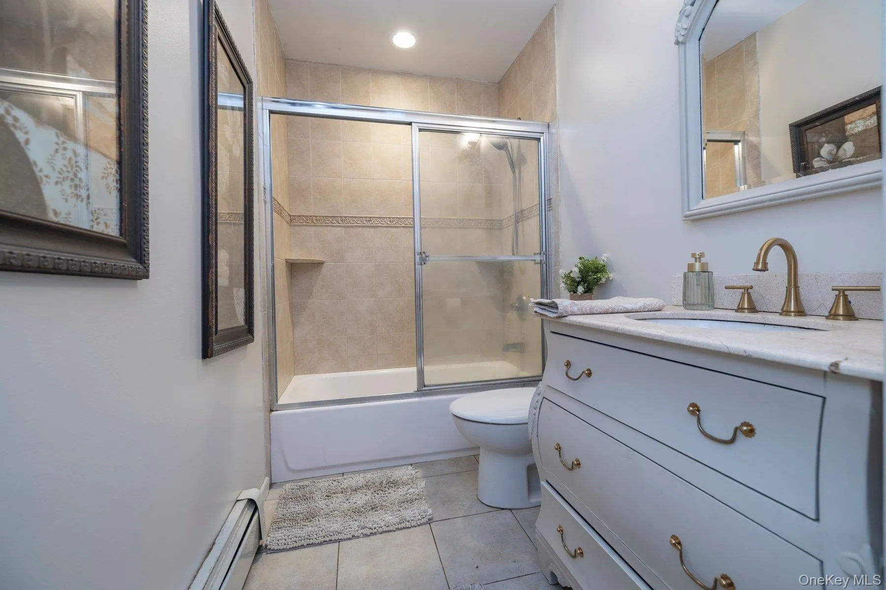 Bathroom featuring vanity, a baseboard heating unit, light tile patterned flooring, and bath / shower combo with glass door Bathroom featuring vanity, a baseboard heating unit, light tile patterned flooring, and bath / shower combo with glass door