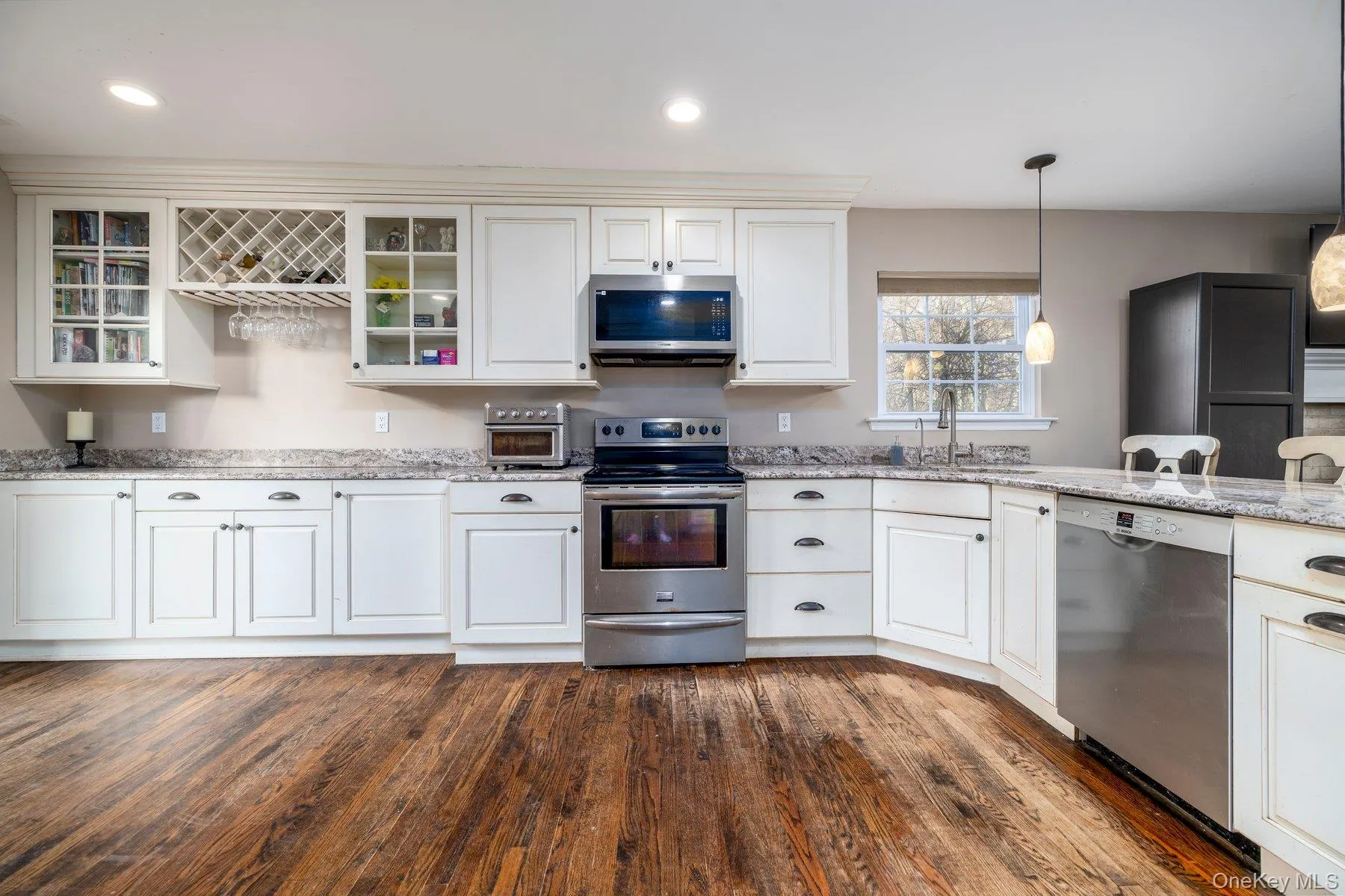 Kitchen with stainless steel appliances, light stone countertops, white cabinetry, dark wood-style flooring, and recessed lighting Kitchen with stainless steel appliances, light stone countertops, white cabinetry, dark wood-style flooring, and recessed lighting