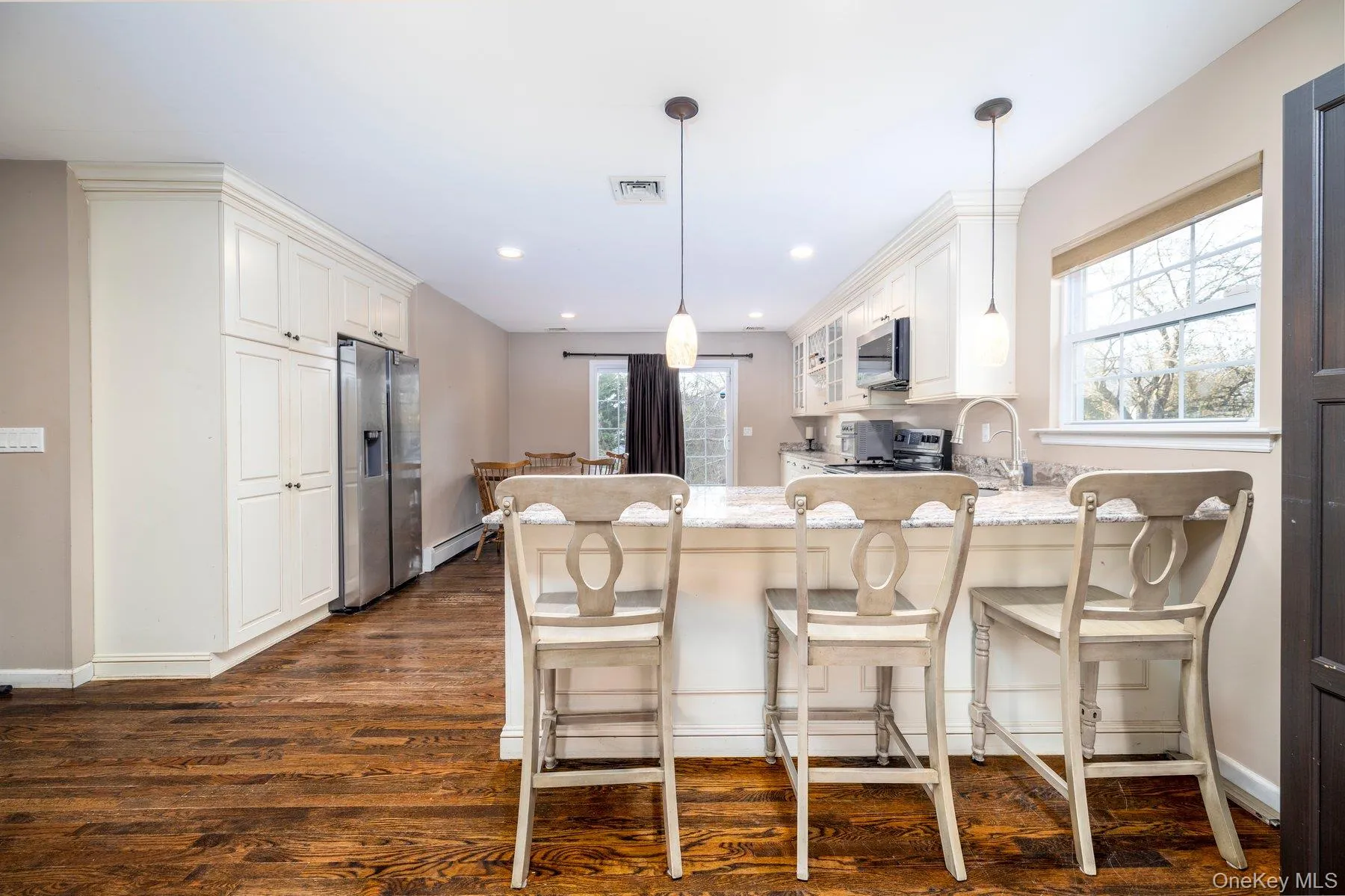 Kitchen with white cabinetry, a kitchen bar, stainless steel appliances, a peninsula, and dark wood finished floors Kitchen with white cabinetry, a kitchen bar, stainless steel appliances, a peninsula, and dark wood finished floors