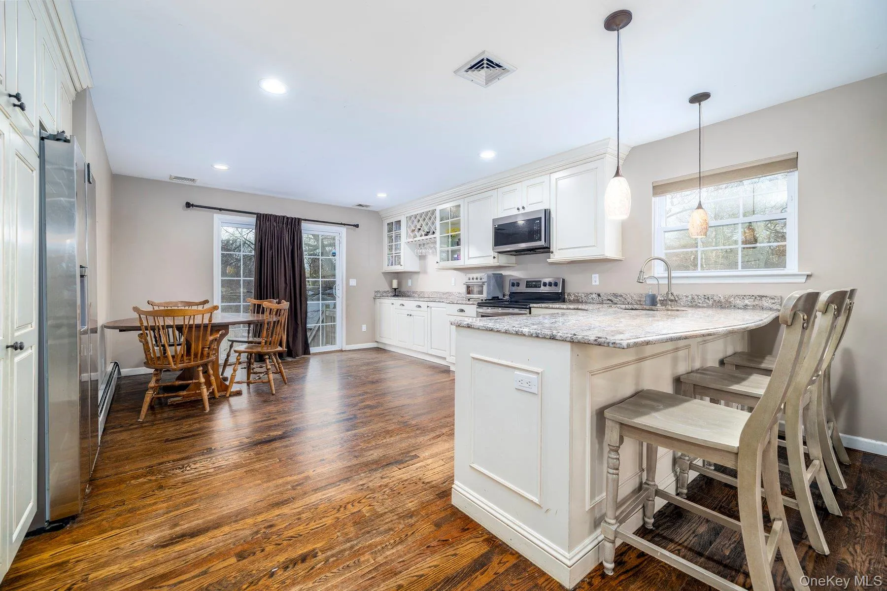 Kitchen with glass insert cabinets, white cabinets, a breakfast bar, appliances with stainless steel finishes, and pendant lighting Kitchen with glass insert cabinets, white cabinets, a breakfast bar, appliances with stainless steel finishes, and pendant lighting