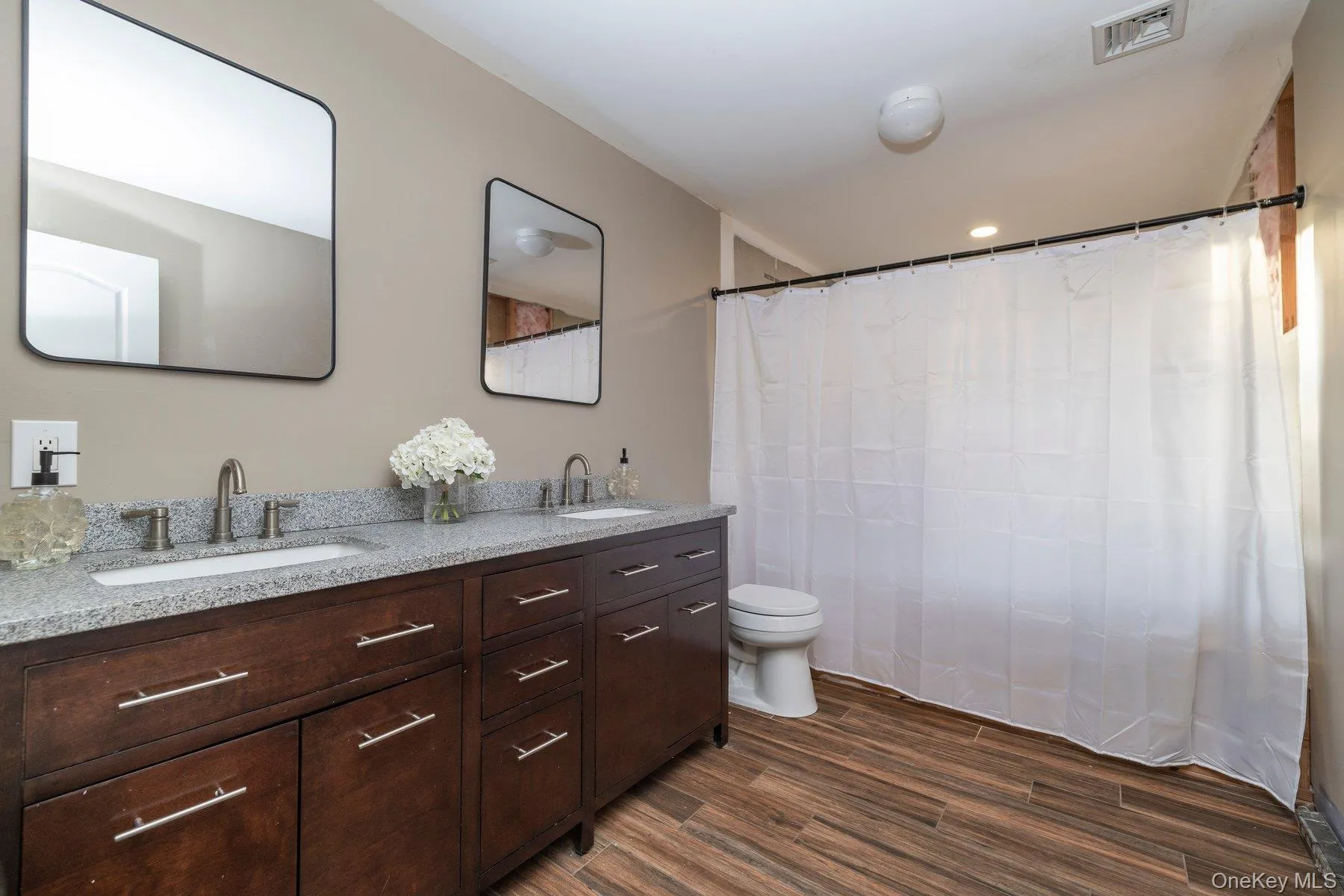 Bathroom with double vanity, dark wood-style flooring, curtained shower, and recessed lighting Bathroom with double vanity, dark wood-style flooring, curtained shower, and recessed lighting