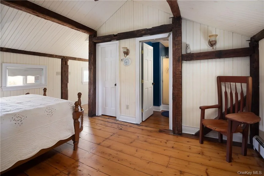 Bedroom featuring hardwood / wood-style flooring, wooden walls, vaulted ceiling with beams. Ensuite bath Bedroom featuring hardwood / wood-style flooring, wooden walls, vaulted ceiling with beams. Ensuite bath