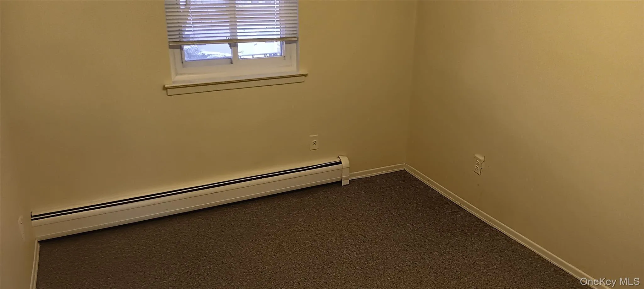 Empty room featuring baseboard heating and dark carpet Empty room featuring baseboard heating and dark carpet