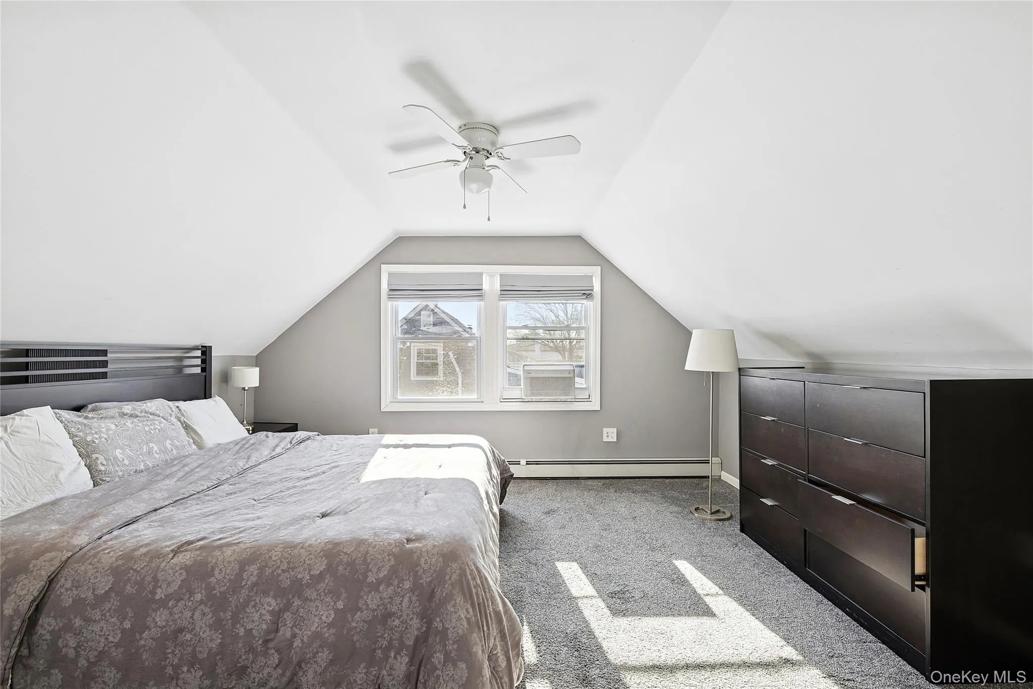Bedroom featuring vaulted ceiling, light colored carpet, ceiling fan, and baseboard heating Bedroom featuring vaulted ceiling, light colored carpet, ceiling fan, and baseboard heating