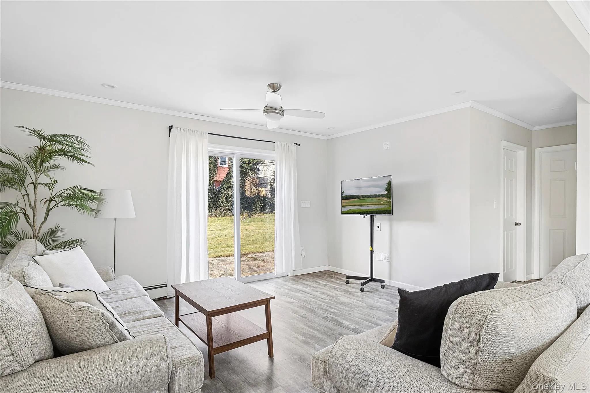 Living room with crown molding, wood finished floors, a baseboard heating unit, and ceiling fan Living room with crown molding, wood finished floors, a baseboard heating unit, and ceiling fan