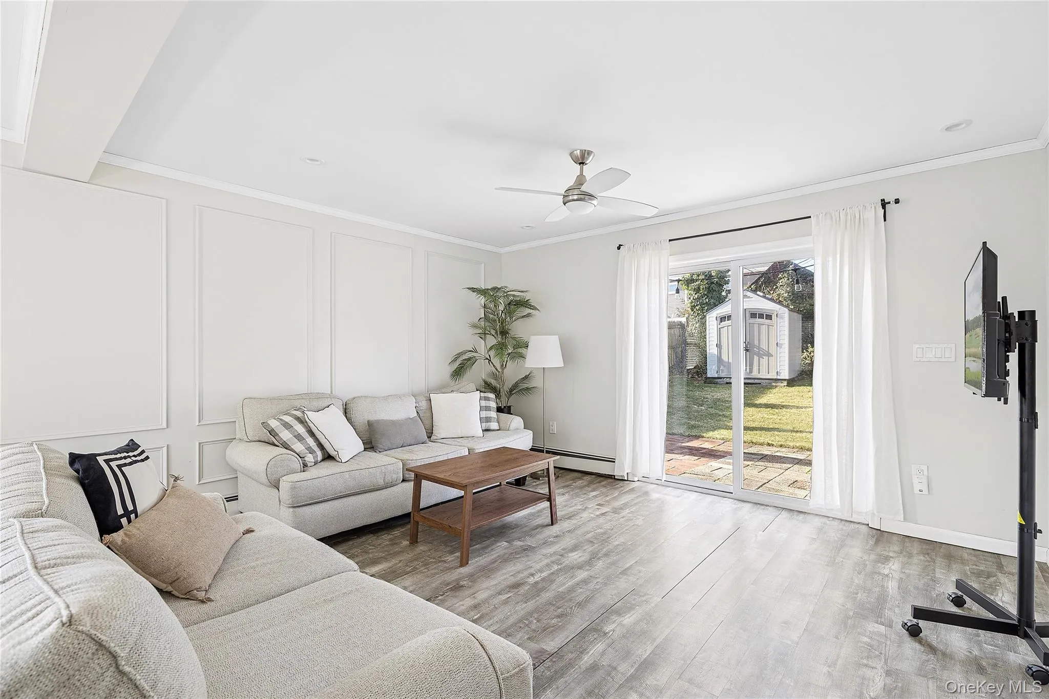 Living area with a decorative wall, a ceiling fan, wood finished floors, crown molding, and a baseboard heating unit Living area with a decorative wall, a ceiling fan, wood finished floors, crown molding, and a baseboard heating unit