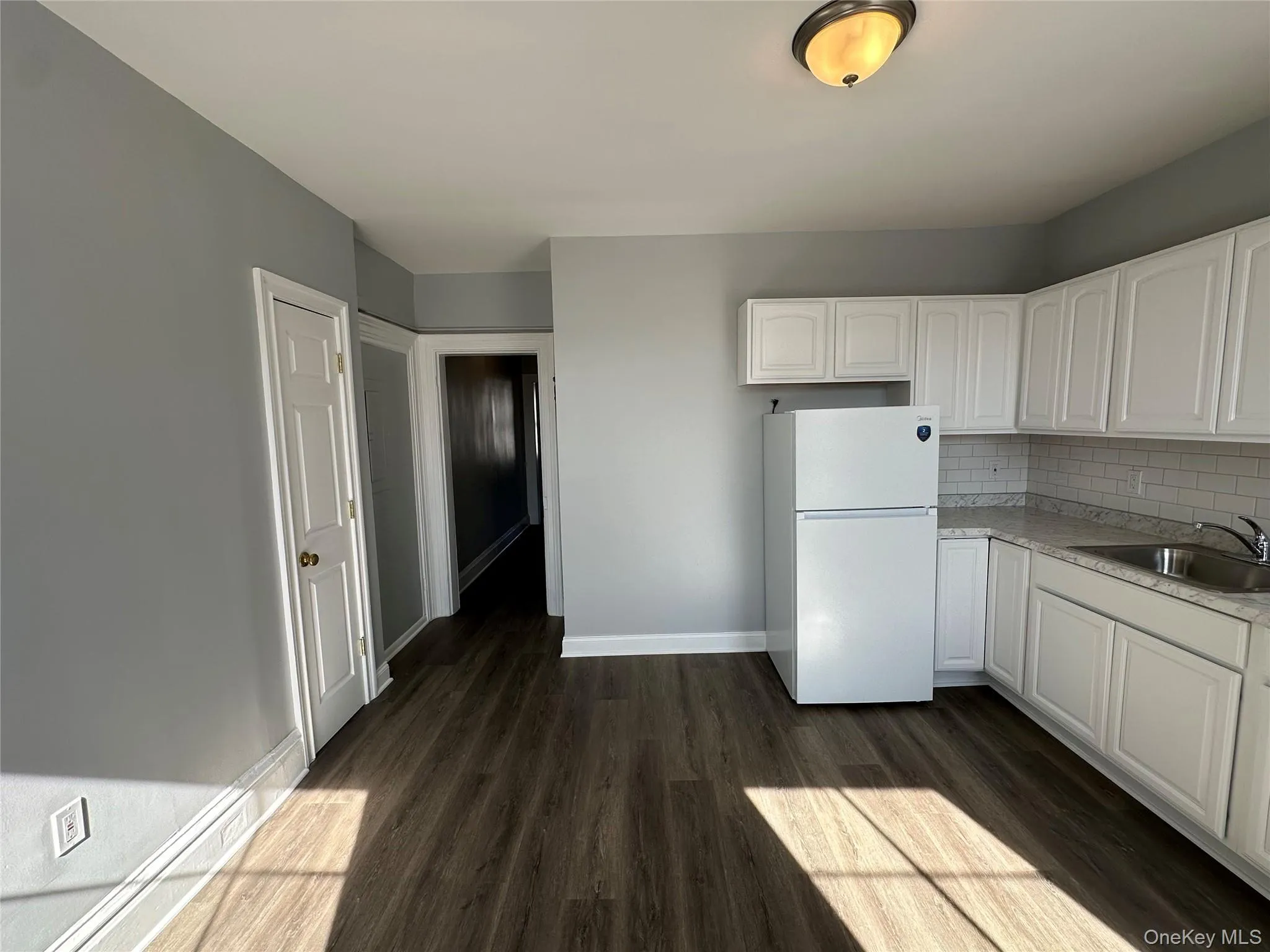 Kitchen featuring white cabinetry, dark hardwood / wood-style flooring, sink, white fridge, and decorative backsplash Kitchen featuring white cabinetry, dark hardwood / wood-style flooring, sink, white fridge, and decorative backsplash