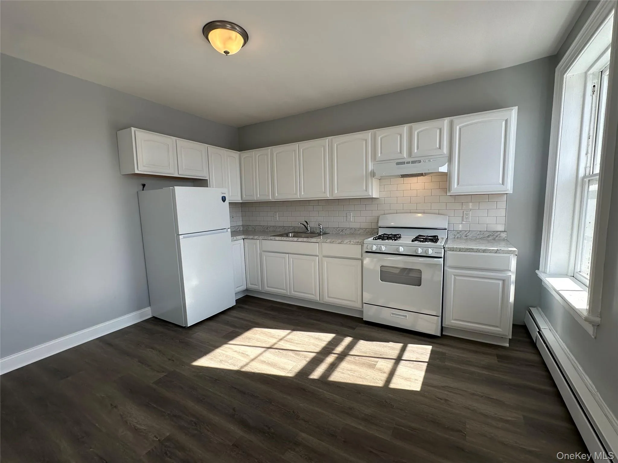 Kitchen featuring white appliances, sink, white cabinetry, a baseboard radiator, and tasteful backsplash Kitchen featuring white appliances, sink, white cabinetry, a baseboard radiator, and tasteful backsplash