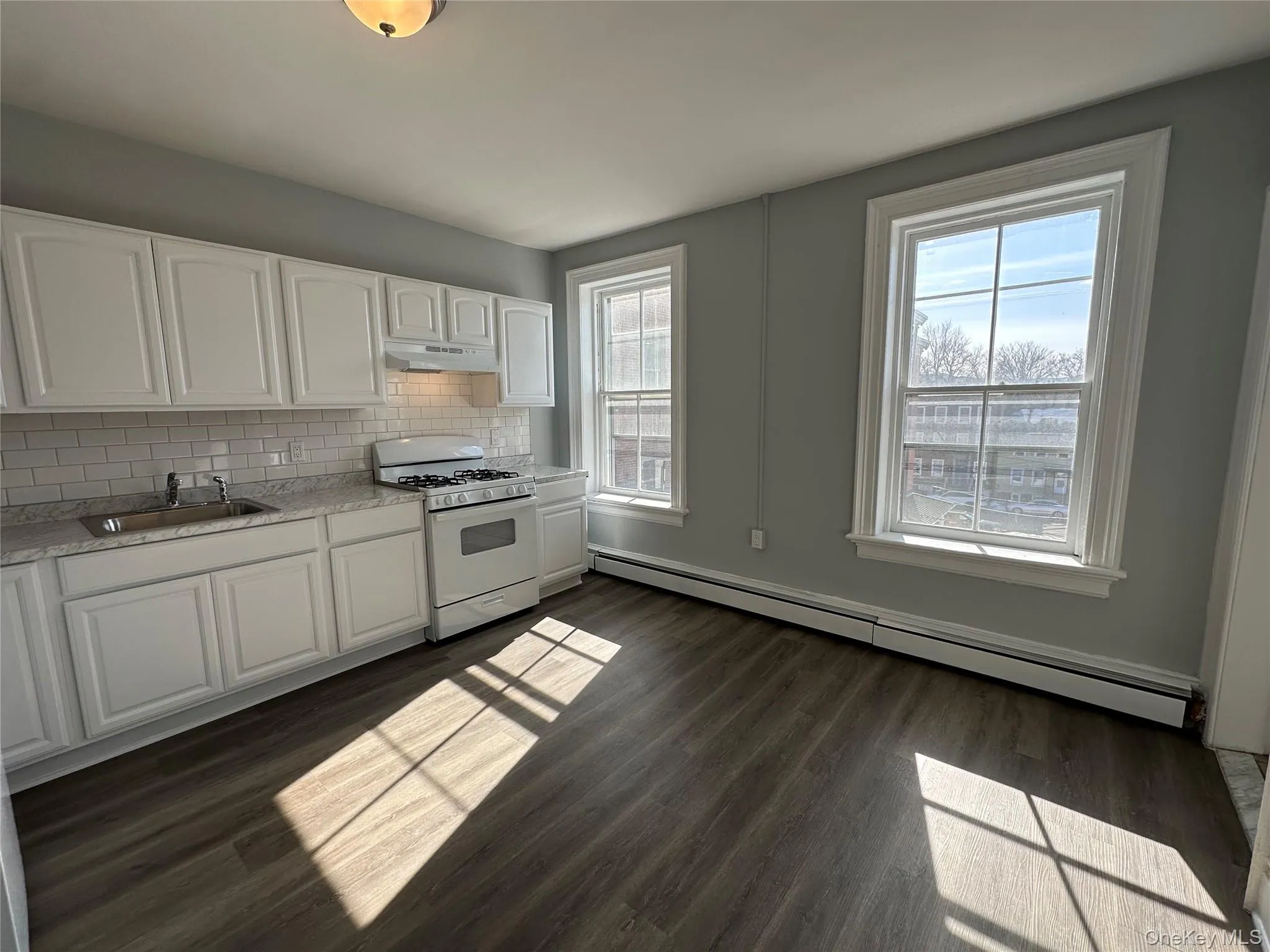 Kitchen with white cabinetry, sink, backsplash, a baseboard radiator, and white range with gas stovetop Kitchen with white cabinetry, sink, backsplash, a baseboard radiator, and white range with gas stovetop