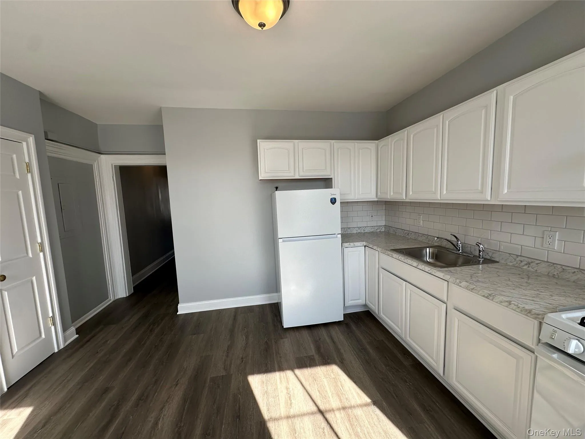 Kitchen with white appliances, sink, backsplash, white cabinetry, and dark hardwood / wood-style flooring Kitchen with white appliances, sink, backsplash, white cabinetry, and dark hardwood / wood-style flooring