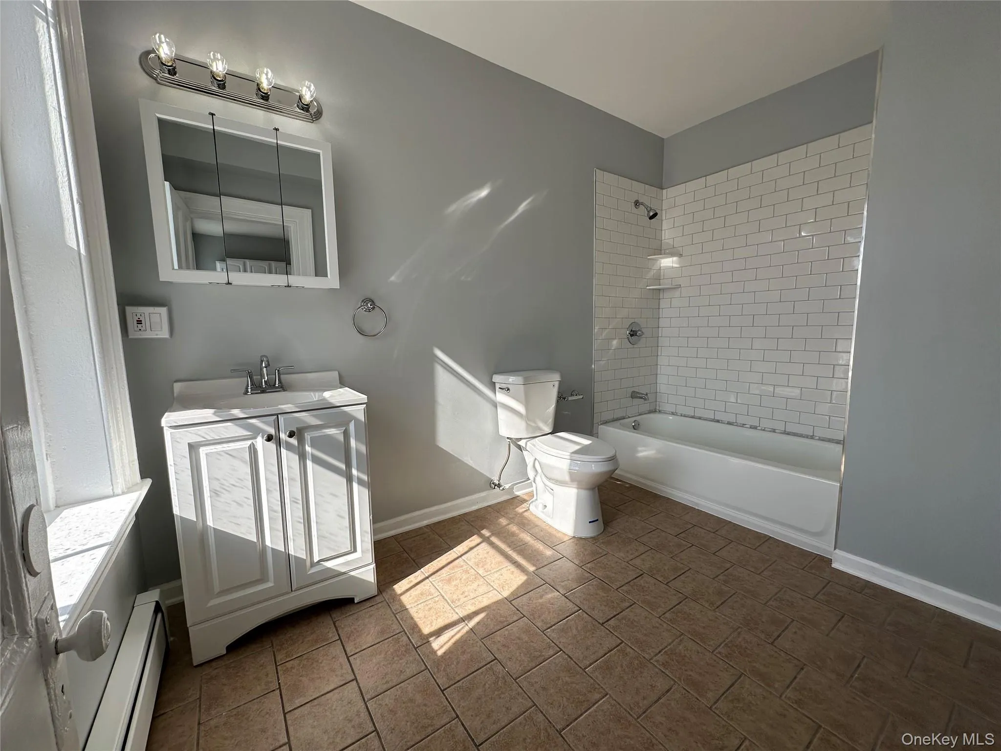 Full bathroom with vanity, a baseboard heating unit, tiled shower / bath combo, tile patterned flooring, and toilet Full bathroom with vanity, a baseboard heating unit, tiled shower / bath combo, tile patterned flooring, and toilet