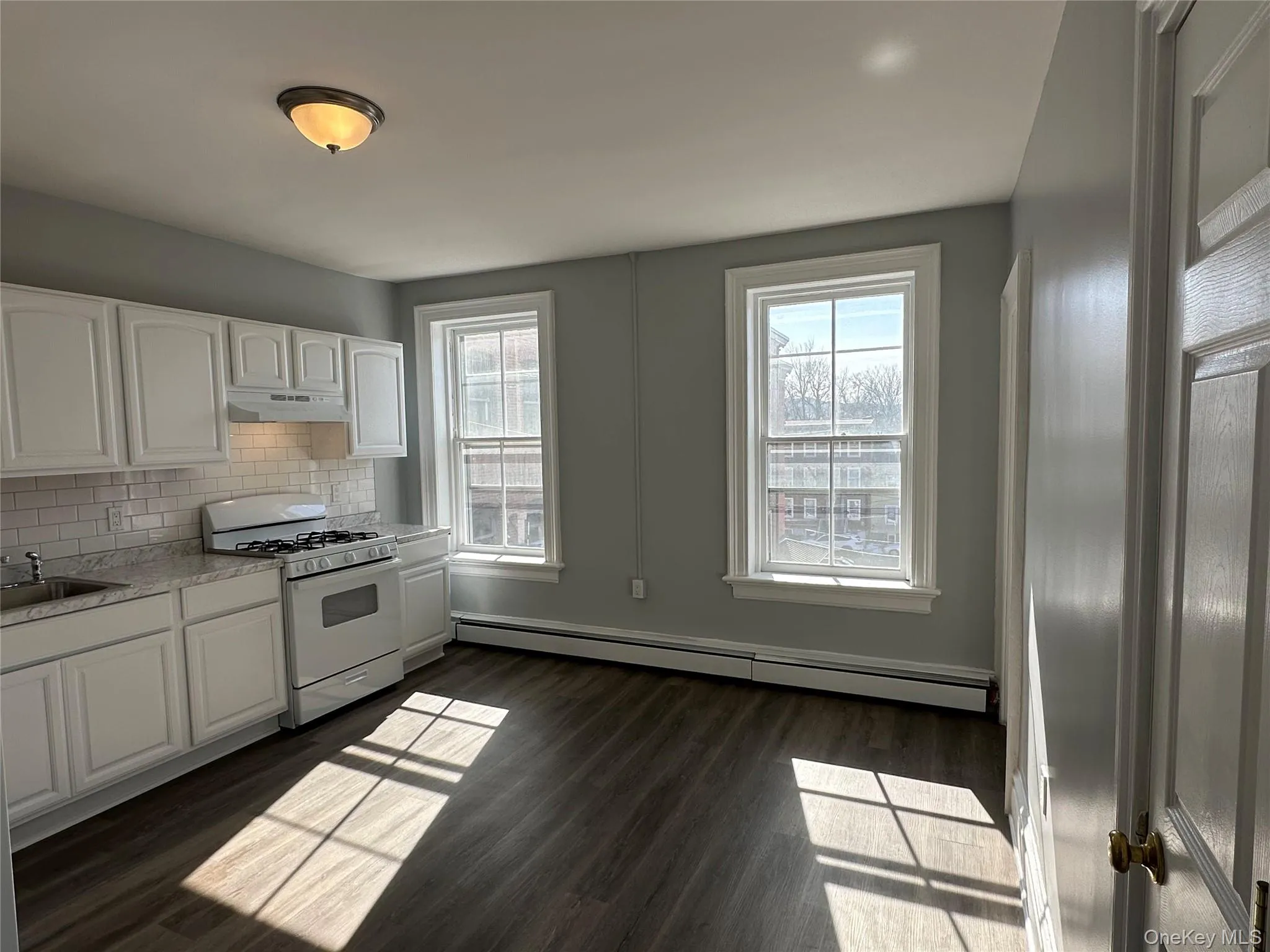 Kitchen with decorative backsplash, white range with gas cooktop, white cabinetry, dark hardwood / wood-style floors, and a baseboard heating unit Kitchen with decorative backsplash, white range with gas cooktop, white cabinetry, dark hardwood / wood-style floors, and a baseboard heating unit