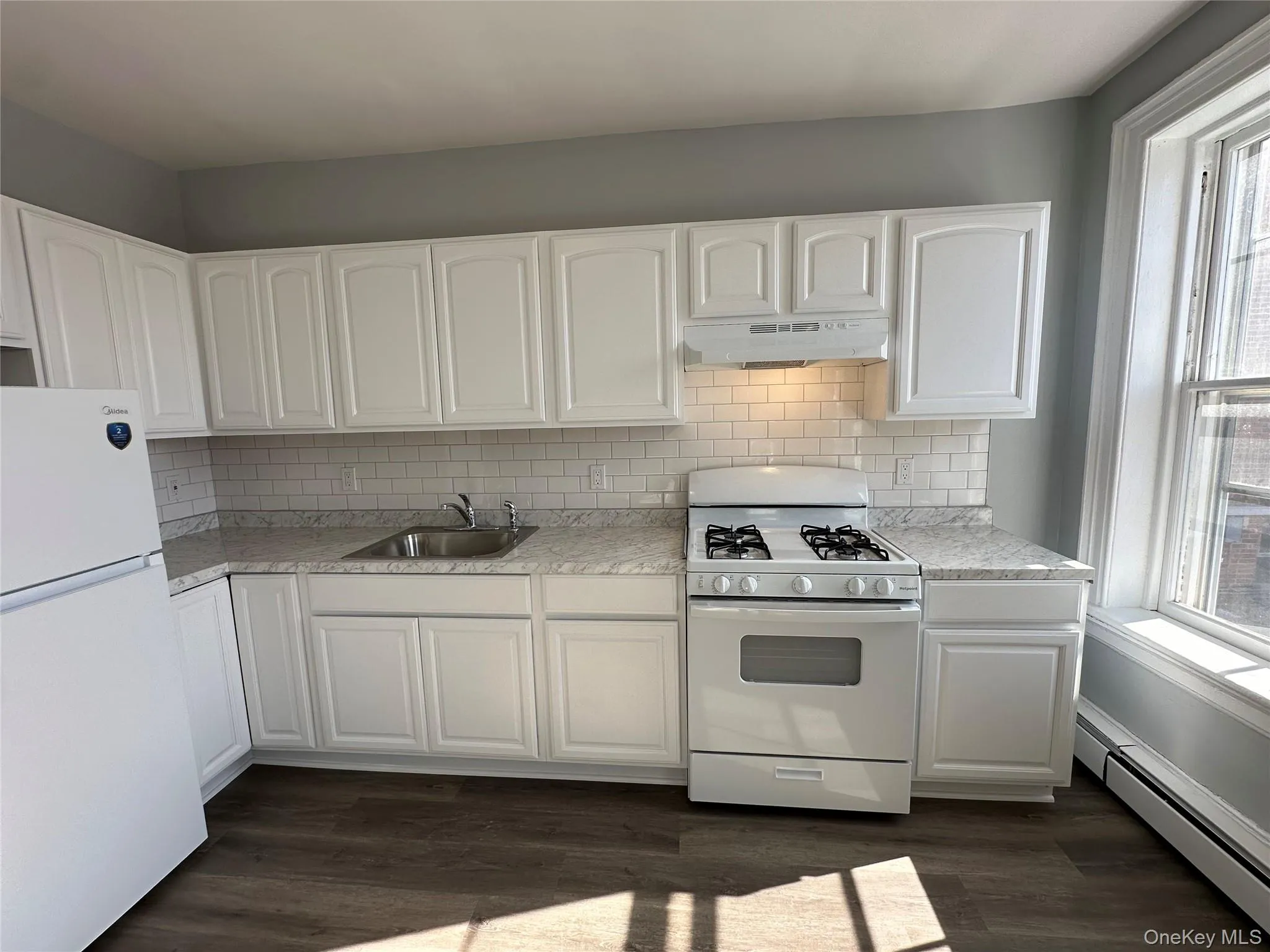 Kitchen featuring white cabinetry, a baseboard heating unit, sink, white appliances, and dark wood-type flooring Kitchen featuring white cabinetry, a baseboard heating unit, sink, white appliances, and dark wood-type flooring