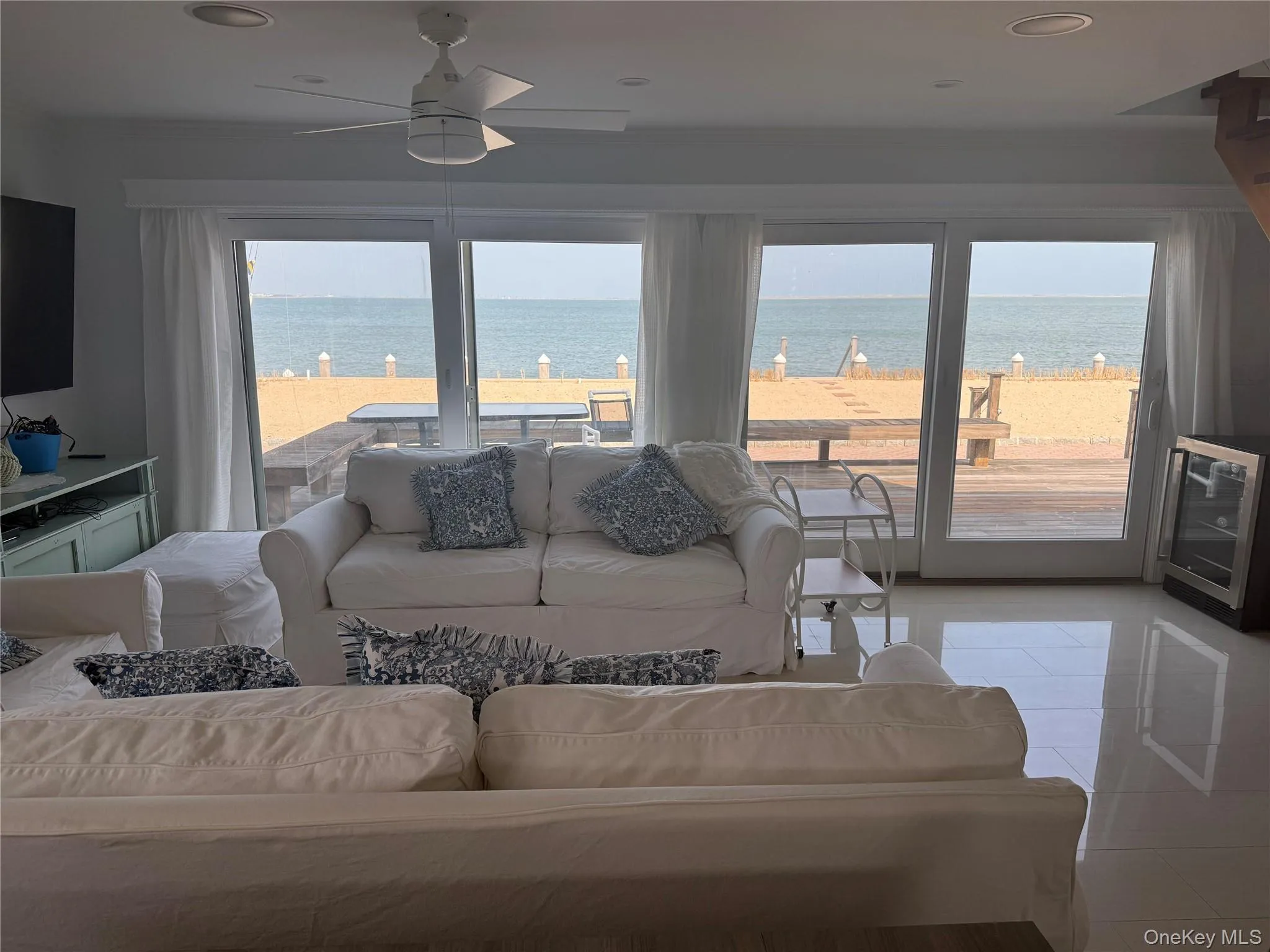 Living room with wine cooler, light tile patterned floors, ornamental molding, ceiling fan, and a water view Living room with wine cooler, light tile patterned floors, ornamental molding, ceiling fan, and a water view