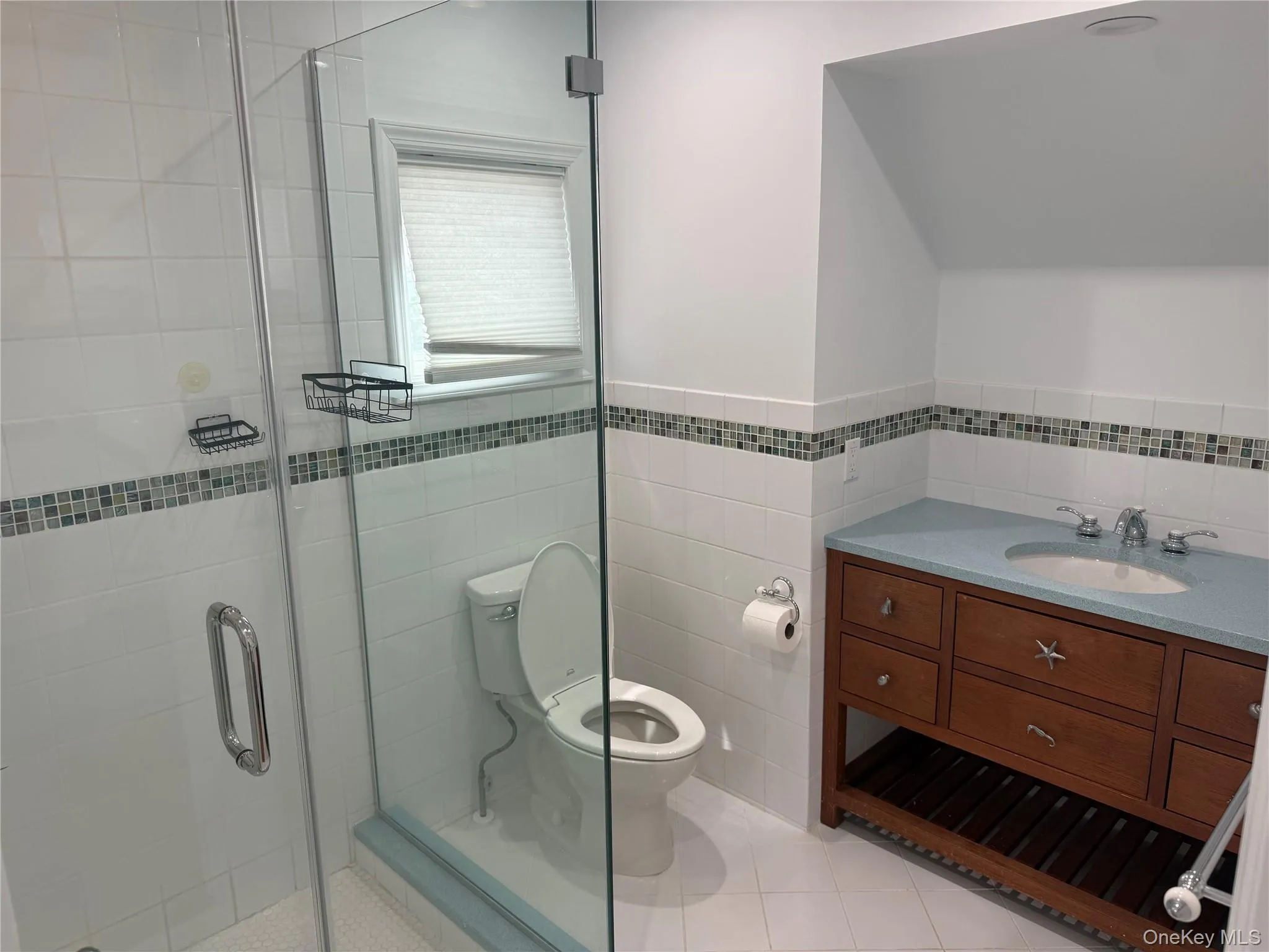 Bathroom featuring toilet, a stall shower, tile patterned floors, tile walls, and vanity Bathroom featuring toilet, a stall shower, tile patterned floors, tile walls, and vanity