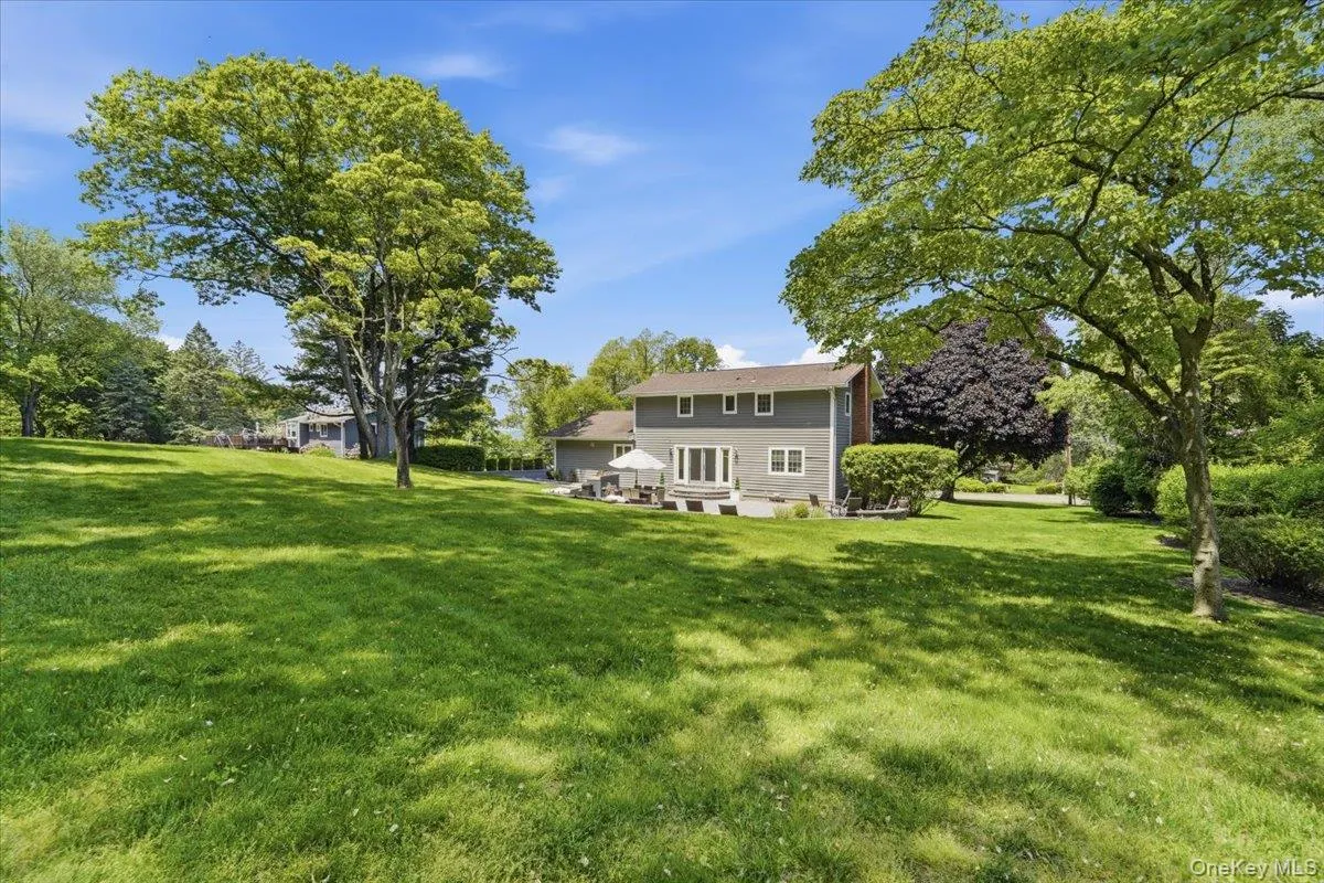 Expansive green lawn with mature trees and a rear property facade featuring multiple windows and a patio Expansive green lawn with mature trees and a rear property facade featuring multiple windows and a patio