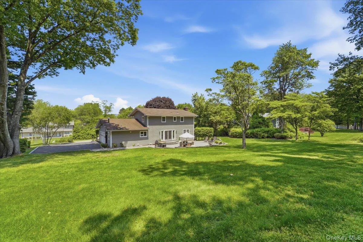 Expansive green lawn surrounds a two-story home with a tan exterior and dark roof Expansive green lawn surrounds a two-story home with a tan exterior and dark roof