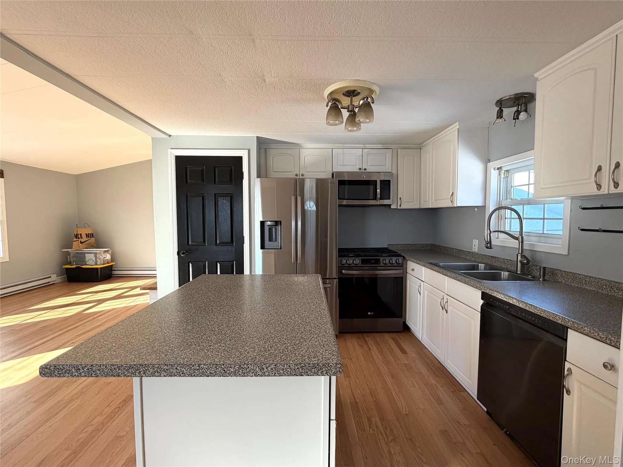 Kitchen with a kitchen island, dark countertops, appliances with stainless steel finishes, and light wood-style floors Kitchen with a kitchen island, dark countertops, appliances with stainless steel finishes, and light wood-style floors