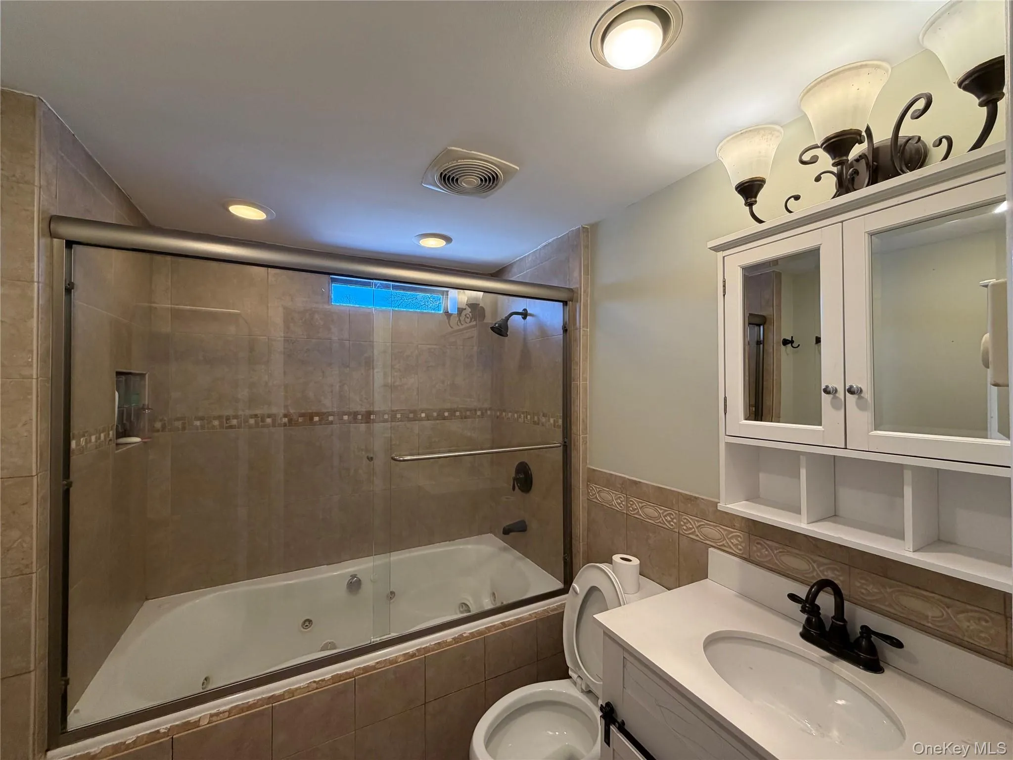 Bathroom with vanity, a combined bath / shower with jetted tub, tile walls, wainscoting, and recessed lighting Bathroom with vanity, a combined bath / shower with jetted tub, tile walls, wainscoting, and recessed lighting