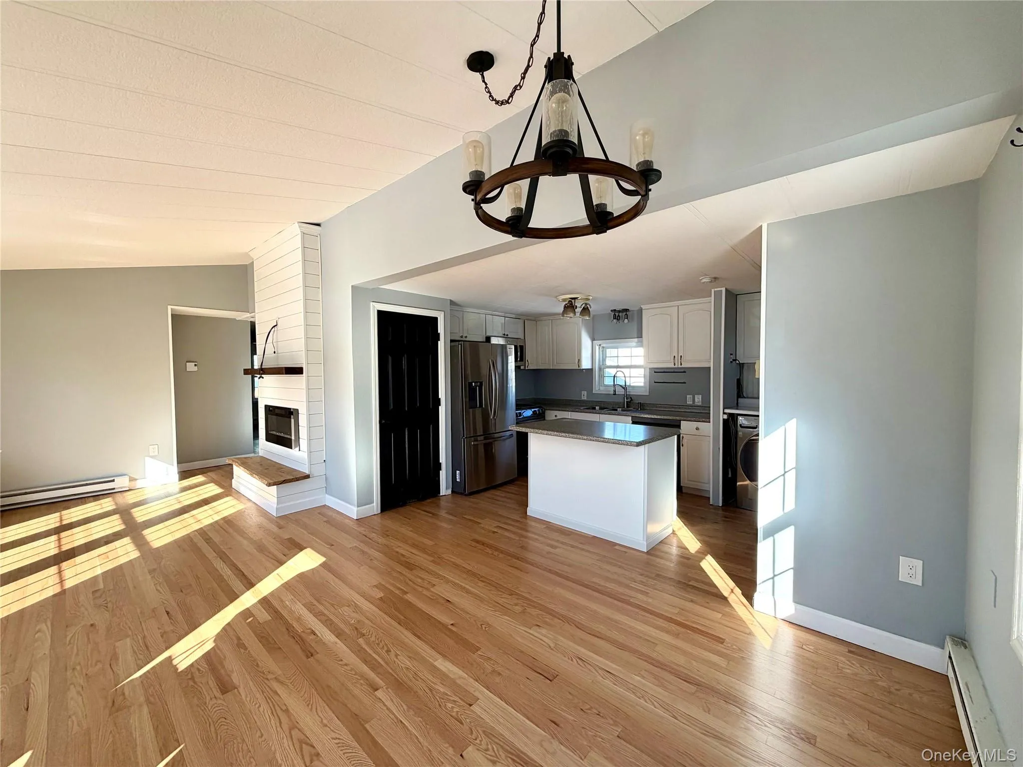 Kitchen with open floor plan, a baseboard heating unit, a large fireplace, decorative light fixtures, and stainless steel fridge Kitchen with open floor plan, a baseboard heating unit, a large fireplace, decorative light fixtures, and stainless steel fridge