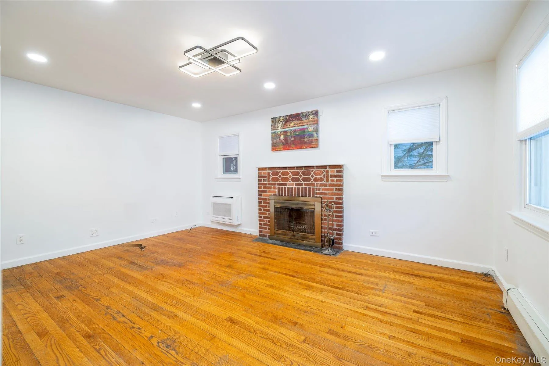 Unfurnished living room with a brick fireplace, a baseboard heating unit, light wood-style flooring, and recessed lighting Unfurnished living room with a brick fireplace, a baseboard heating unit, light wood-style flooring, and recessed lighting