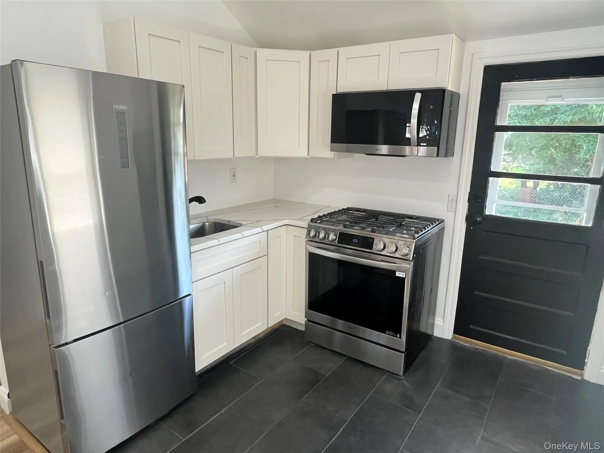 Kitchen with appliances with stainless steel finishes, white cabinetry, dark tile patterned floors, and light stone countertops Kitchen with appliances with stainless steel finishes, white cabinetry, dark tile patterned floors, and light stone countertops