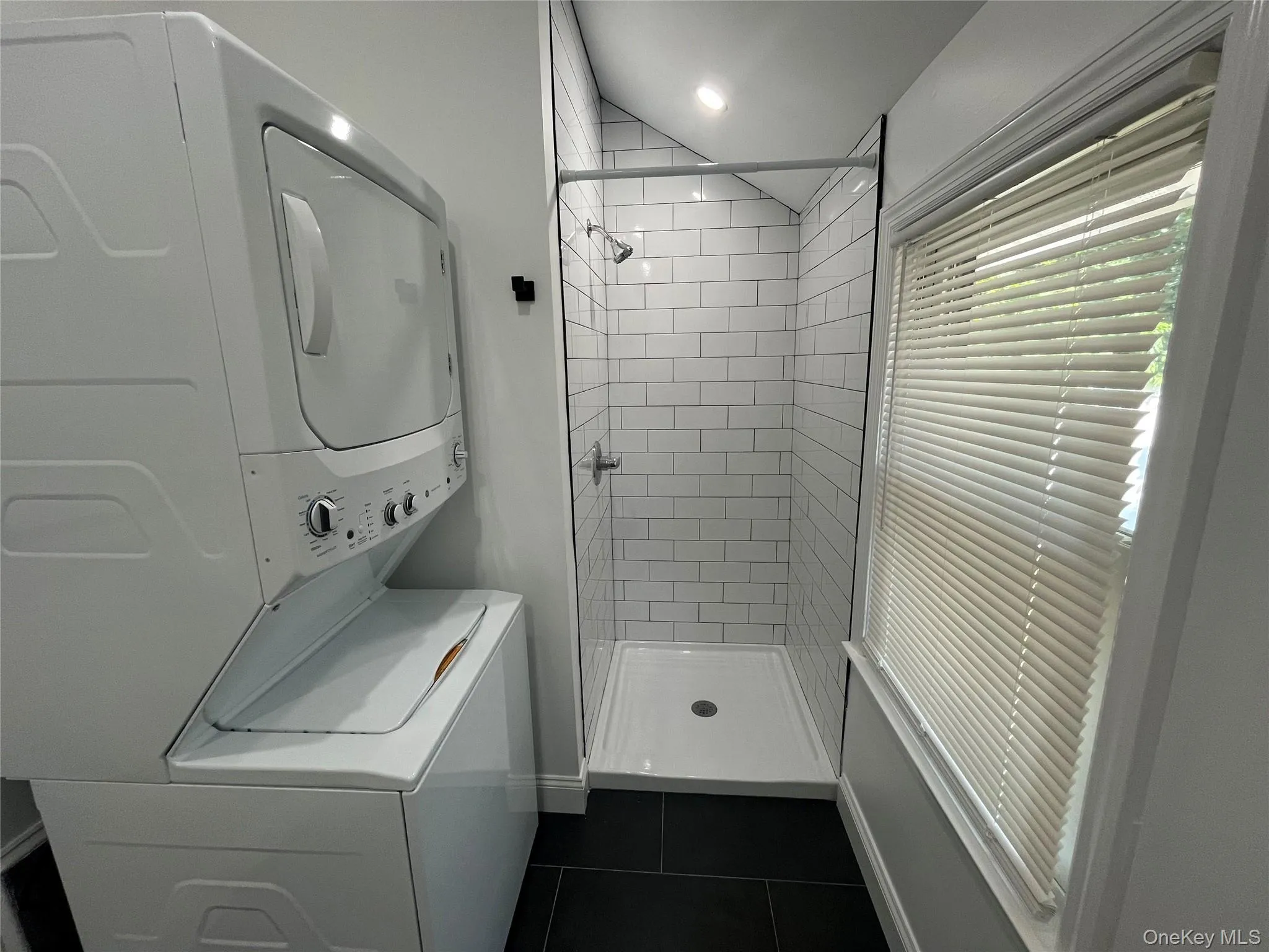 Bathroom featuring stacked washing machine and dryer, a stall shower, dark tile patterned floors, and recessed lighting Bathroom featuring stacked washing machine and dryer, a stall shower, dark tile patterned floors, and recessed lighting