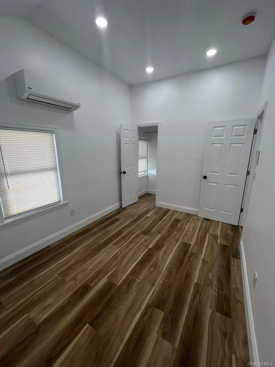 Bedroom featuring dark wood finished floors, a wall mounted AC, recessed lighting, and multiple windows Bedroom featuring dark wood finished floors, a wall mounted AC, recessed lighting, and multiple windows