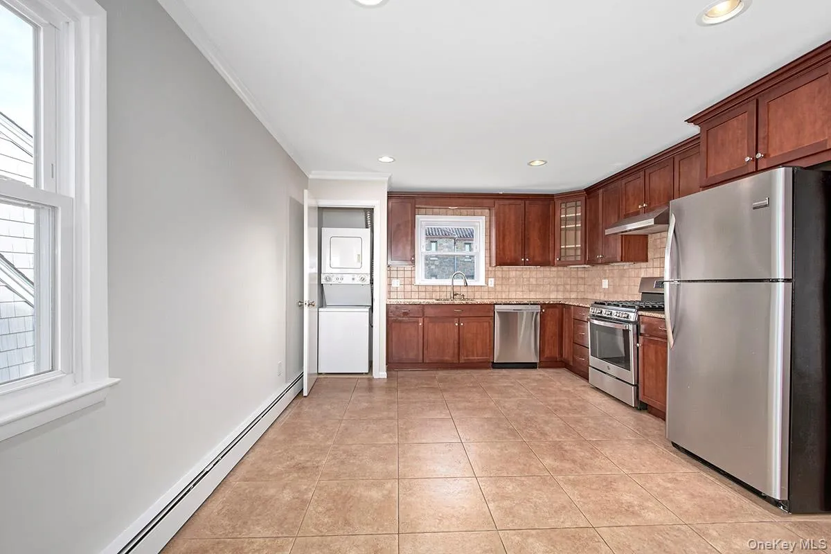 Kitchen with stainless steel appliances, a baseboard heating stacked washer / drying machine, and decorative backsplash Kitchen with stainless steel appliances, a baseboard heating stacked washer / drying machine, and decorative backsplash