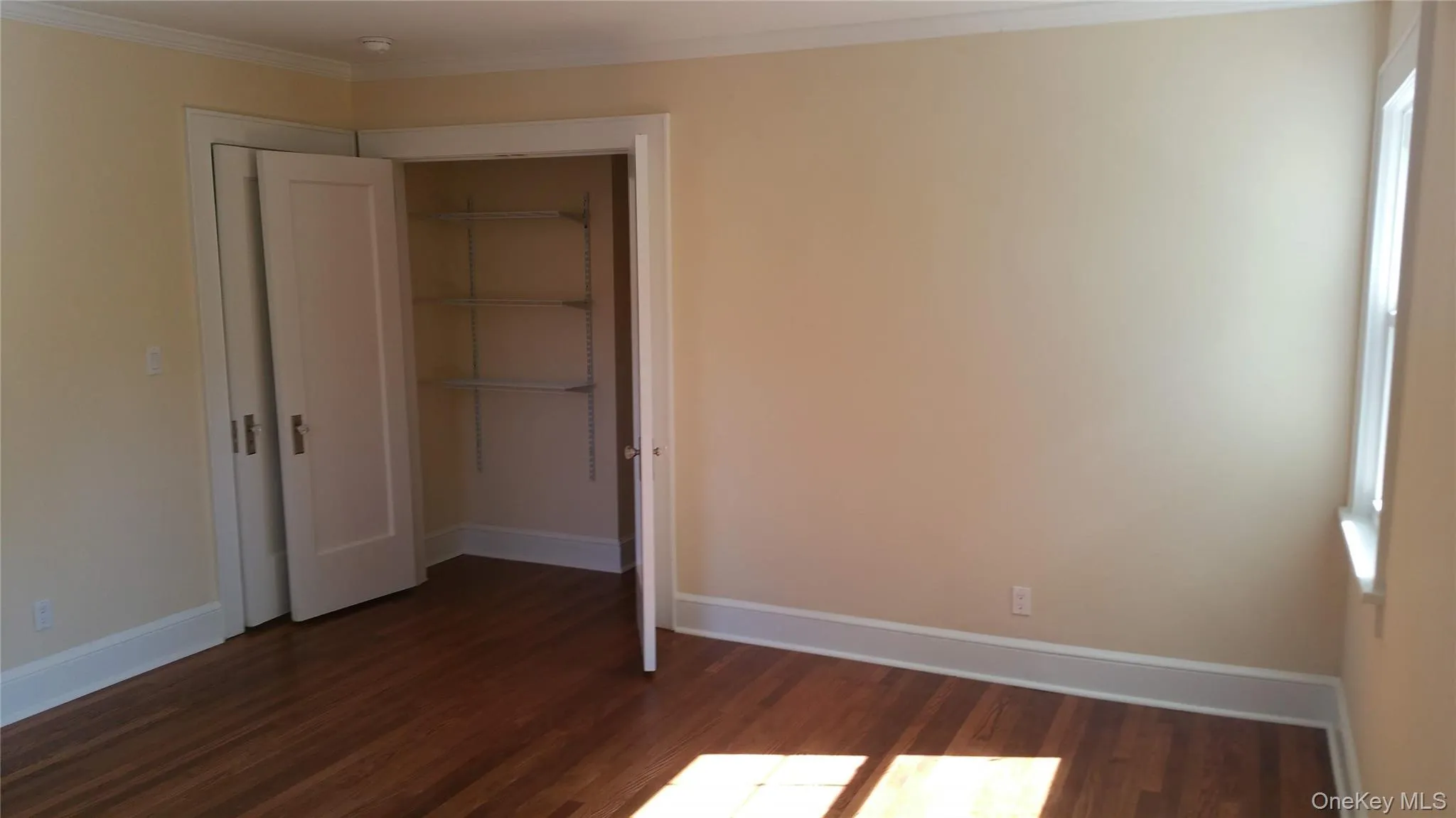 Unfurnished bedroom featuring dark wood-style flooring, ornamental molding, and a closet Unfurnished bedroom featuring dark wood-style flooring, ornamental molding, and a closet