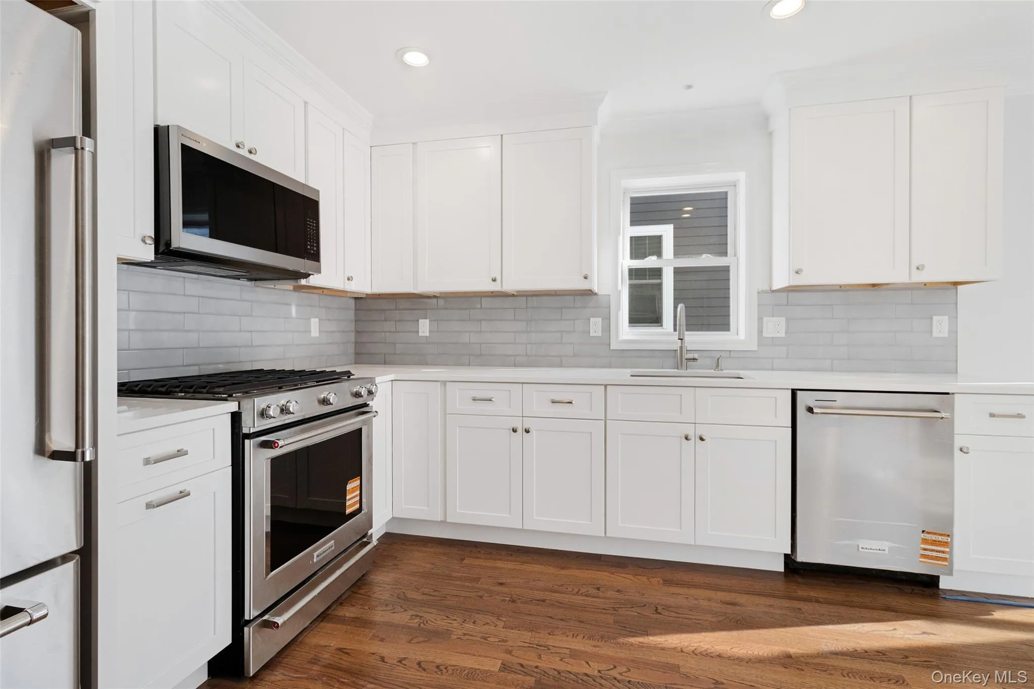 Kitchen with stainless steel appliances, dark wood-style flooring, white cabinets, backsplash, and recessed lighting Kitchen with stainless steel appliances, dark wood-style flooring, white cabinets, backsplash, and recessed lighting