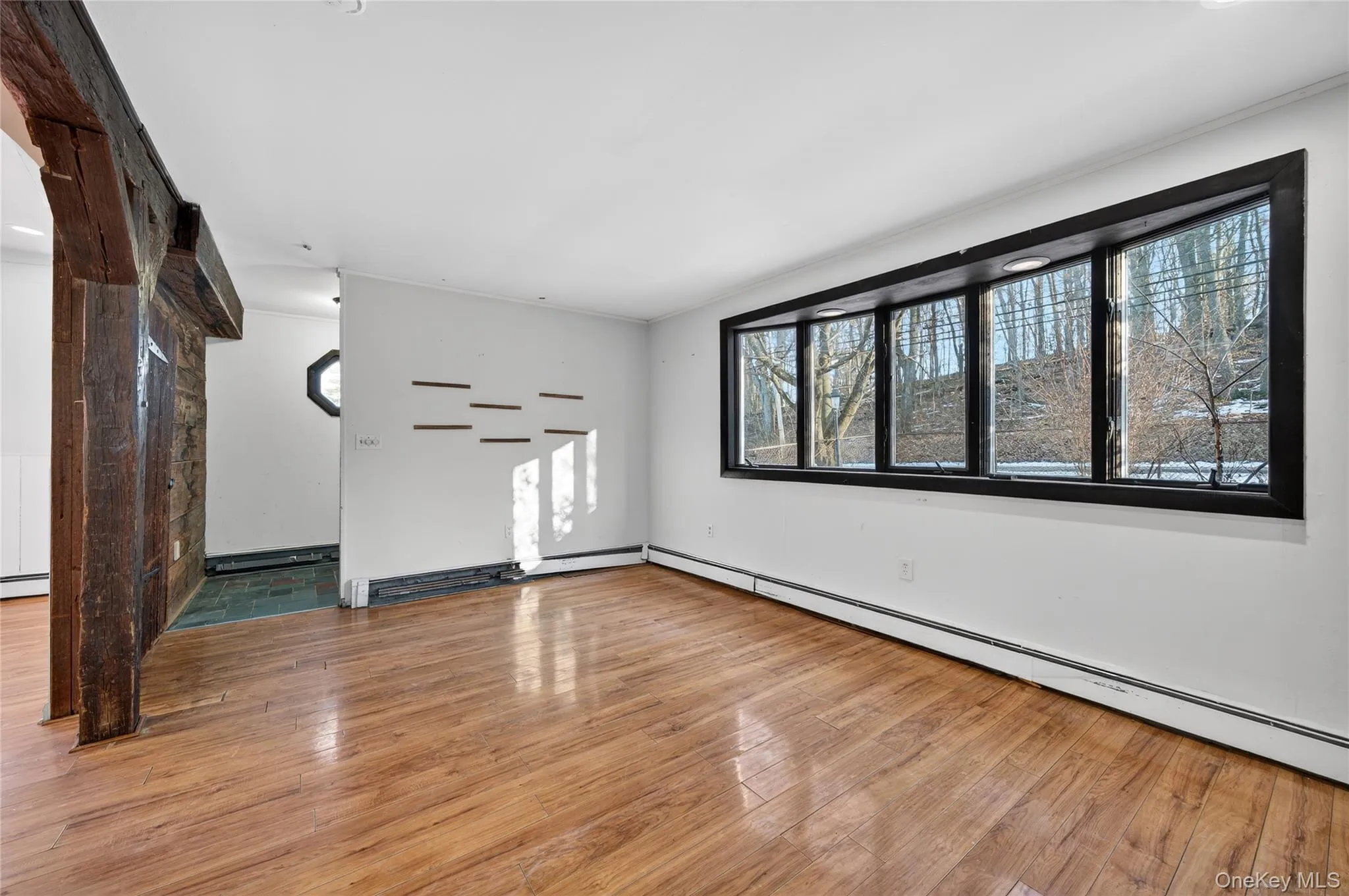 Unfurnished living room featuring baseboard heating, light wood-style floors, and ornamental molding Unfurnished living room featuring baseboard heating, light wood-style floors, and ornamental molding