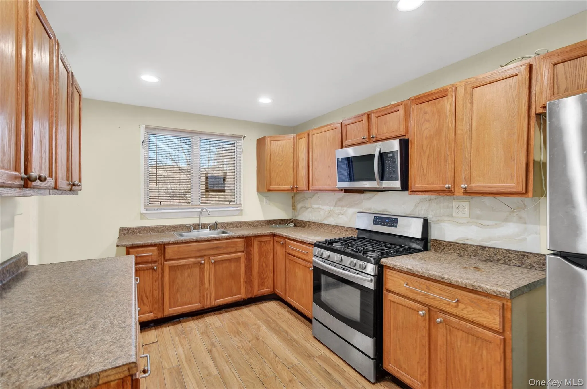 Kitchen with appliances with stainless steel finishes, light wood finished floors, recessed lighting, tasteful backsplash, and brown cabinetry Kitchen with appliances with stainless steel finishes, light wood finished floors, recessed lighting, tasteful backsplash, and brown cabinetry
