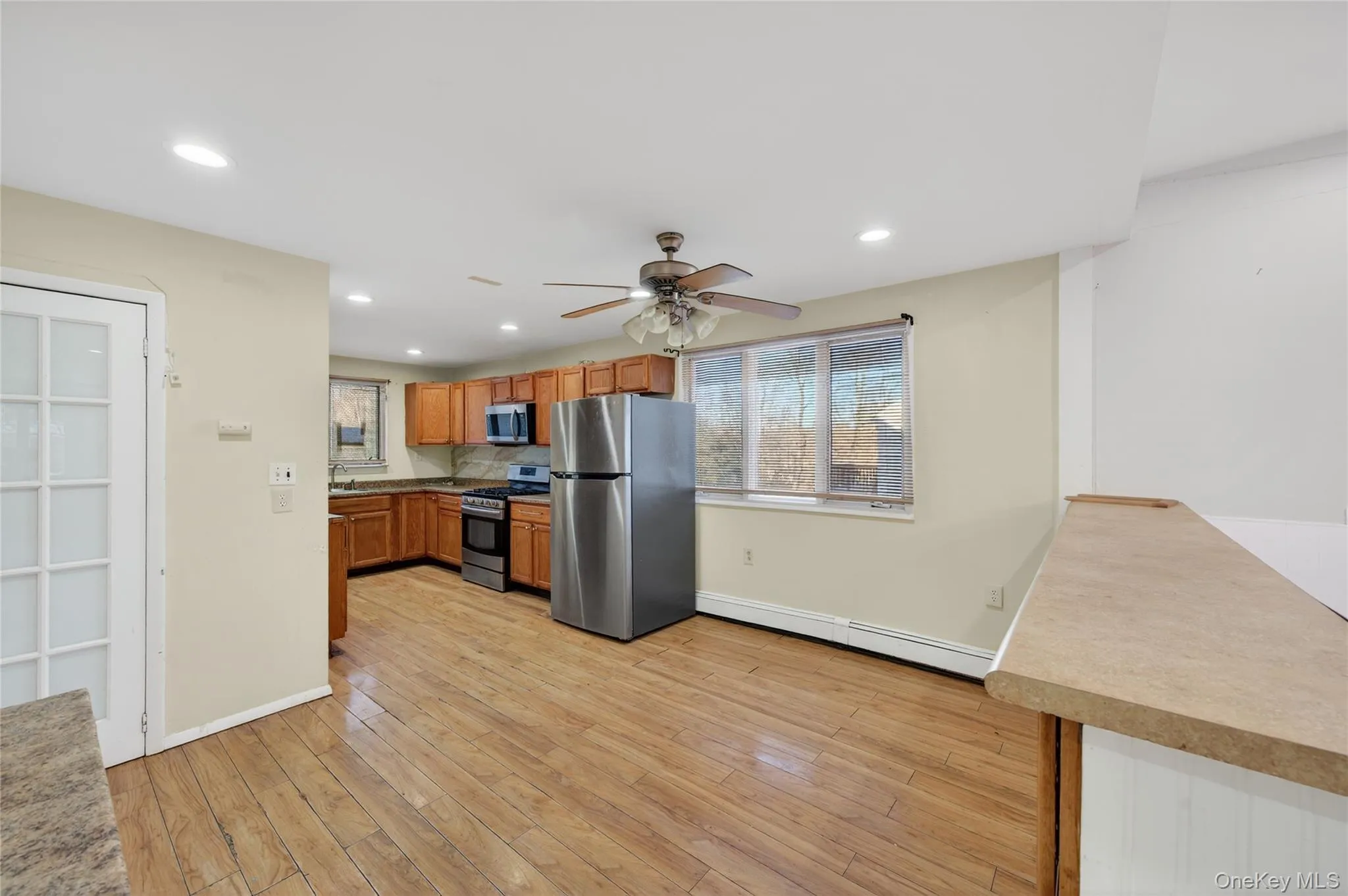 Kitchen featuring brown cabinetry, stainless steel appliances, healthy amount of natural light, a baseboard heating unit, and recessed lighting Kitchen featuring brown cabinetry, stainless steel appliances, healthy amount of natural light, a baseboard heating unit, and recessed lighting