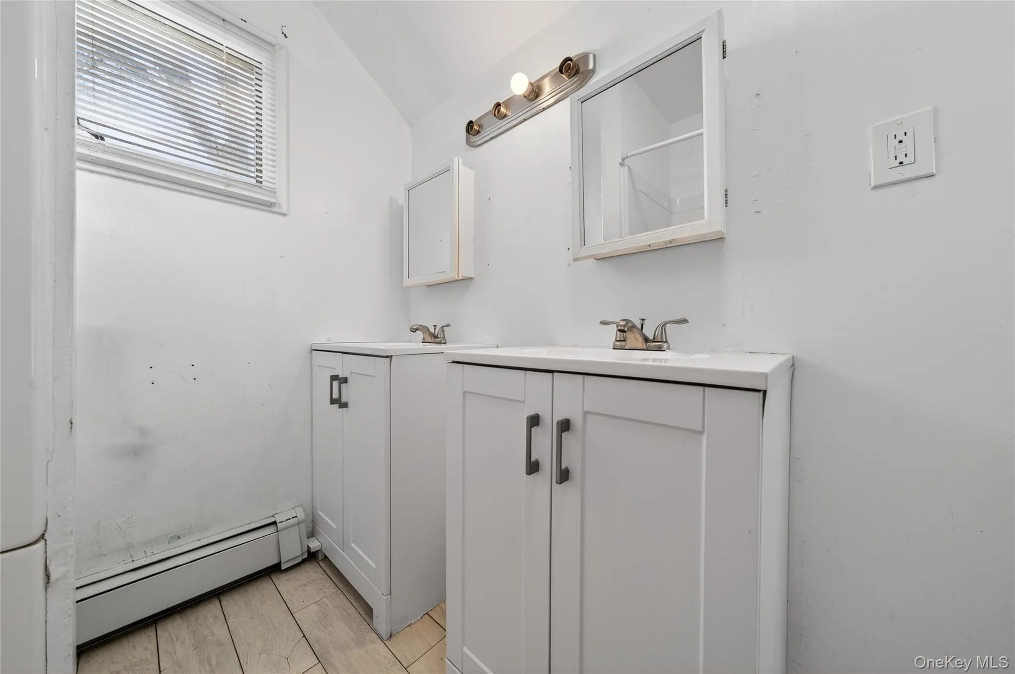 Full bathroom featuring baseboard heating, two vanities, and lofted ceiling Full bathroom featuring baseboard heating, two vanities, and lofted ceiling