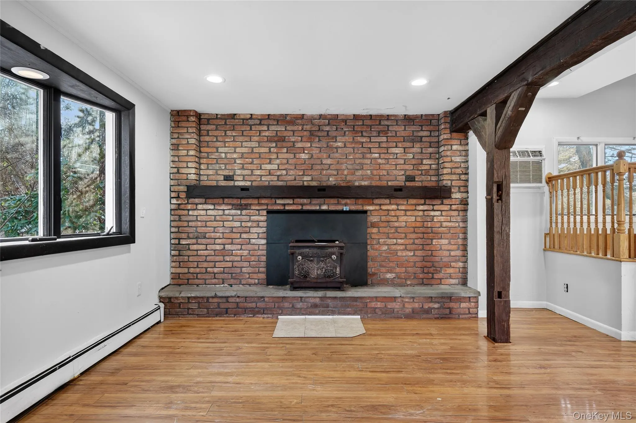 Unfurnished living room with a baseboard heating unit, wood finished floors, and a wood stove Unfurnished living room with a baseboard heating unit, wood finished floors, and a wood stove