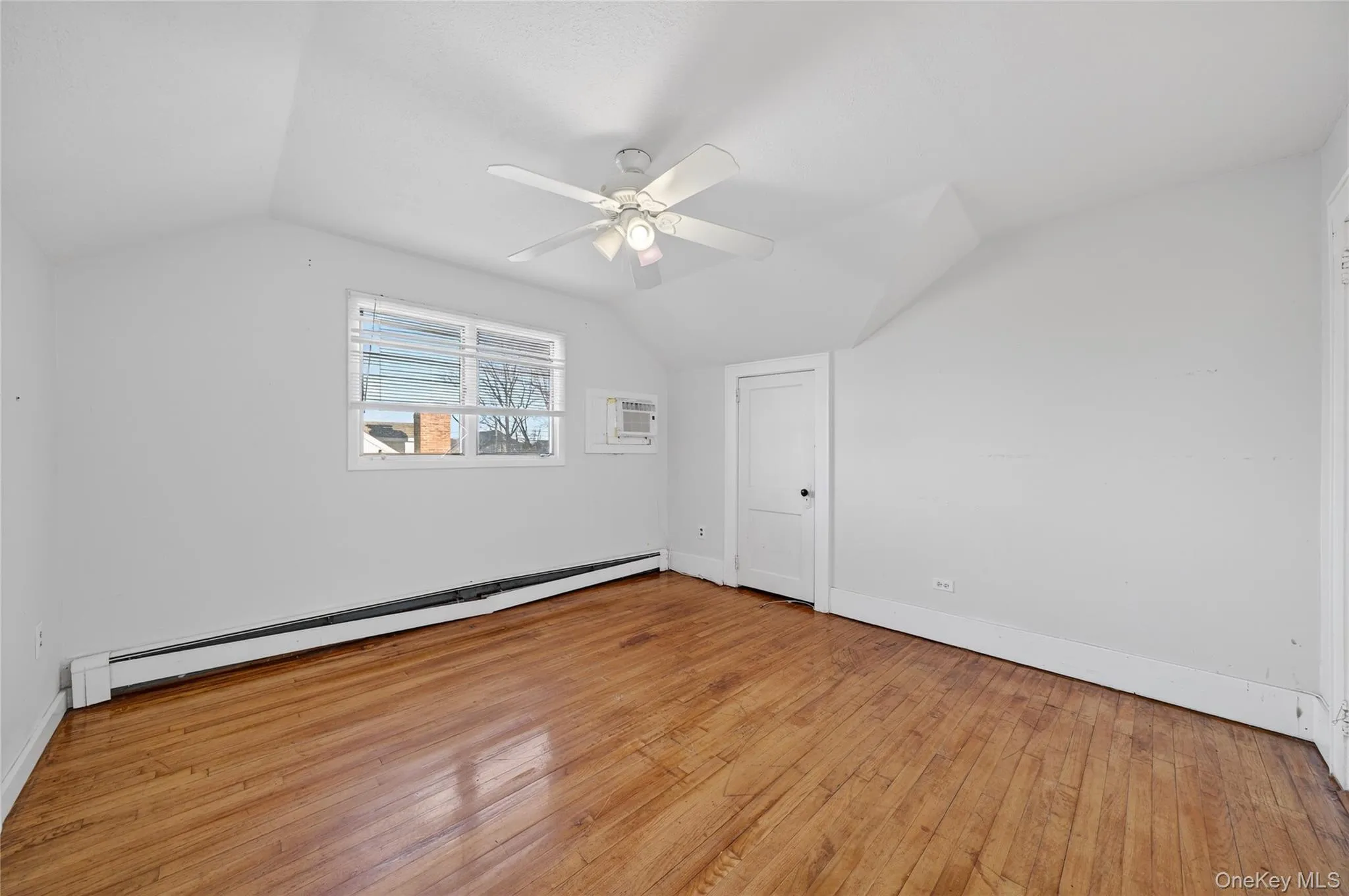 Additional living space with baseboard heating, lofted ceiling, light wood-type flooring, a ceiling fan, and a wall mounted air conditioner Additional living space with baseboard heating, lofted ceiling, light wood-type flooring, a ceiling fan, and a wall mounted air conditioner