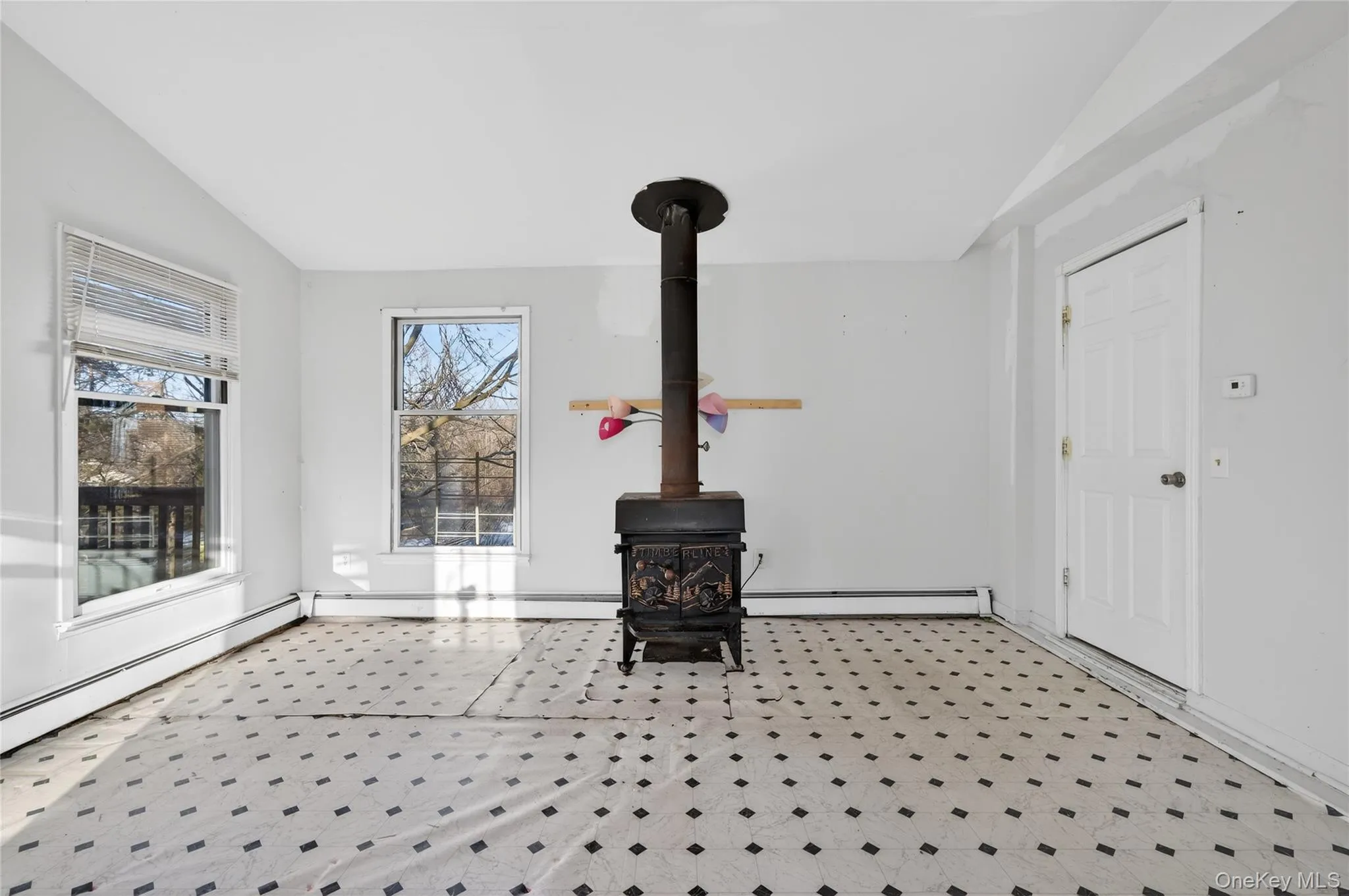 Unfurnished living room with a wood stove, vaulted ceiling, light floors, and a baseboard heating unit Unfurnished living room with a wood stove, vaulted ceiling, light floors, and a baseboard heating unit
