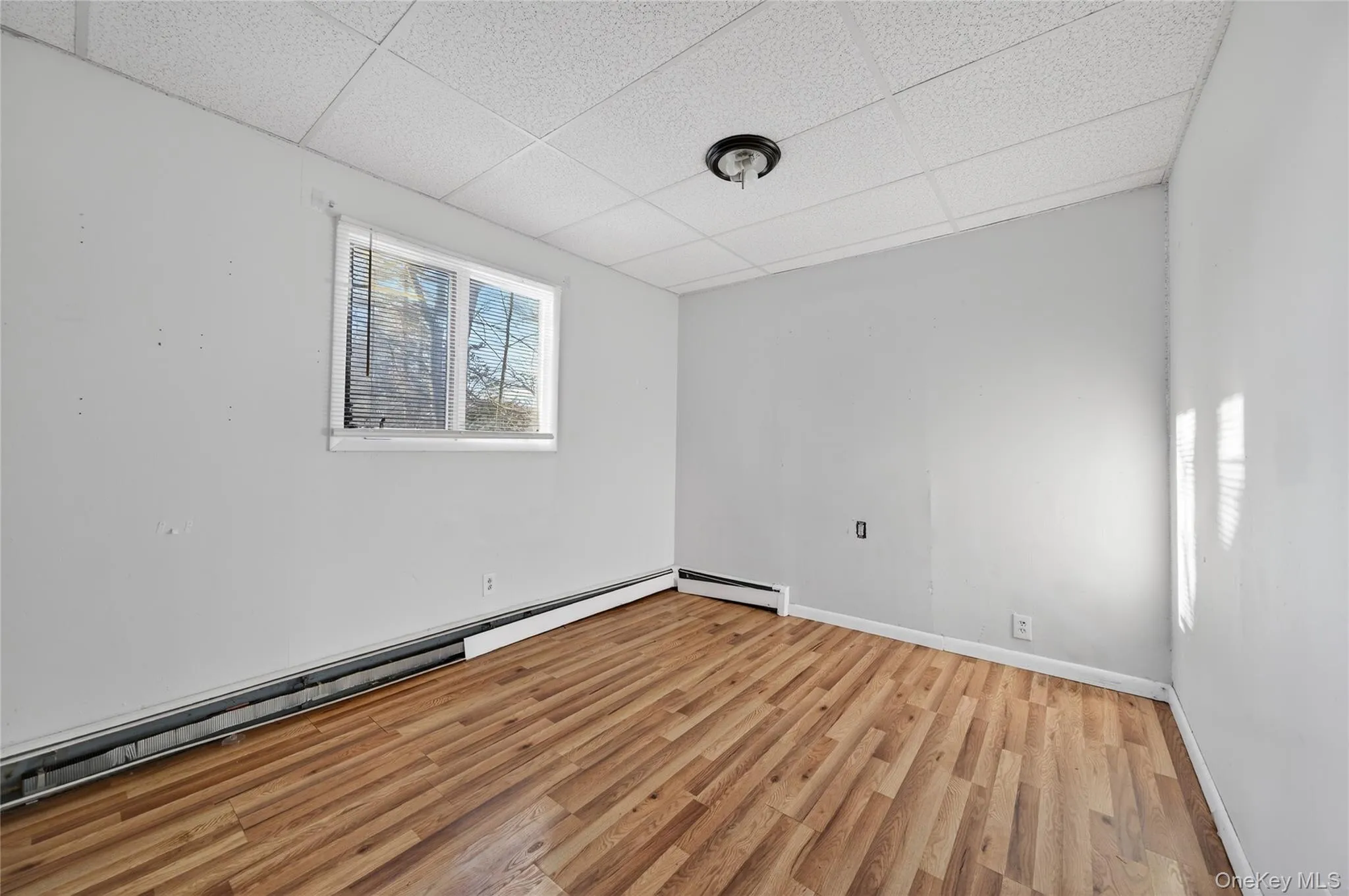 Unfurnished room with a paneled ceiling, a baseboard heating unit, and wood finished floors Unfurnished room with a paneled ceiling, a baseboard heating unit, and wood finished floors